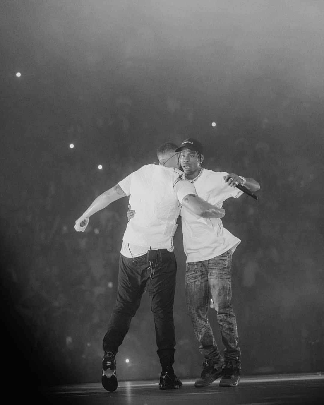 Drake 桌布 壁紙 — 兩個男人在煙霧瀰漫的演唱會舞台上，在明亮的聚光燈下擁抱，身後是模糊的人群。