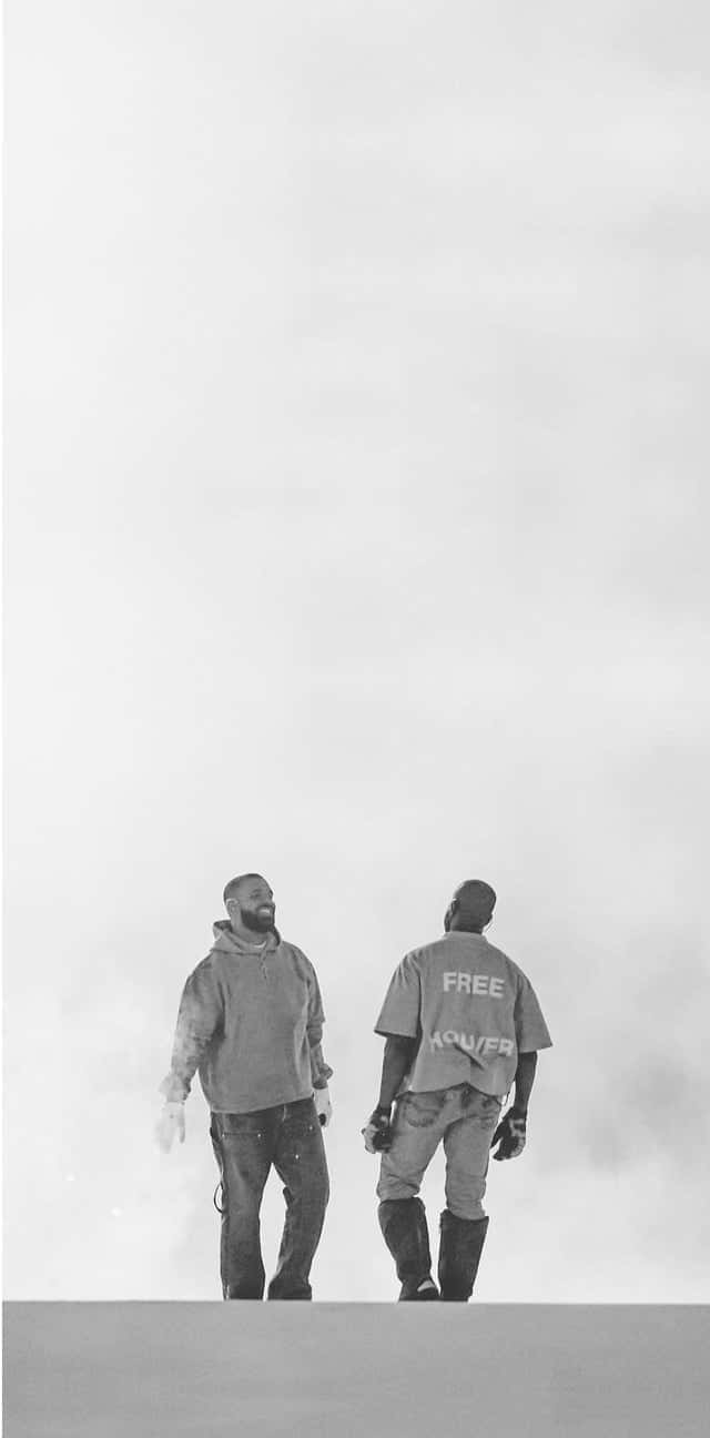 Drake 桌布 壁紙 — 兩個男人背對背站在一個懸崖邊，背景是朦朧的天空，一個穿著連帽衫，另一個穿著背後寫有「free」的襯衫。