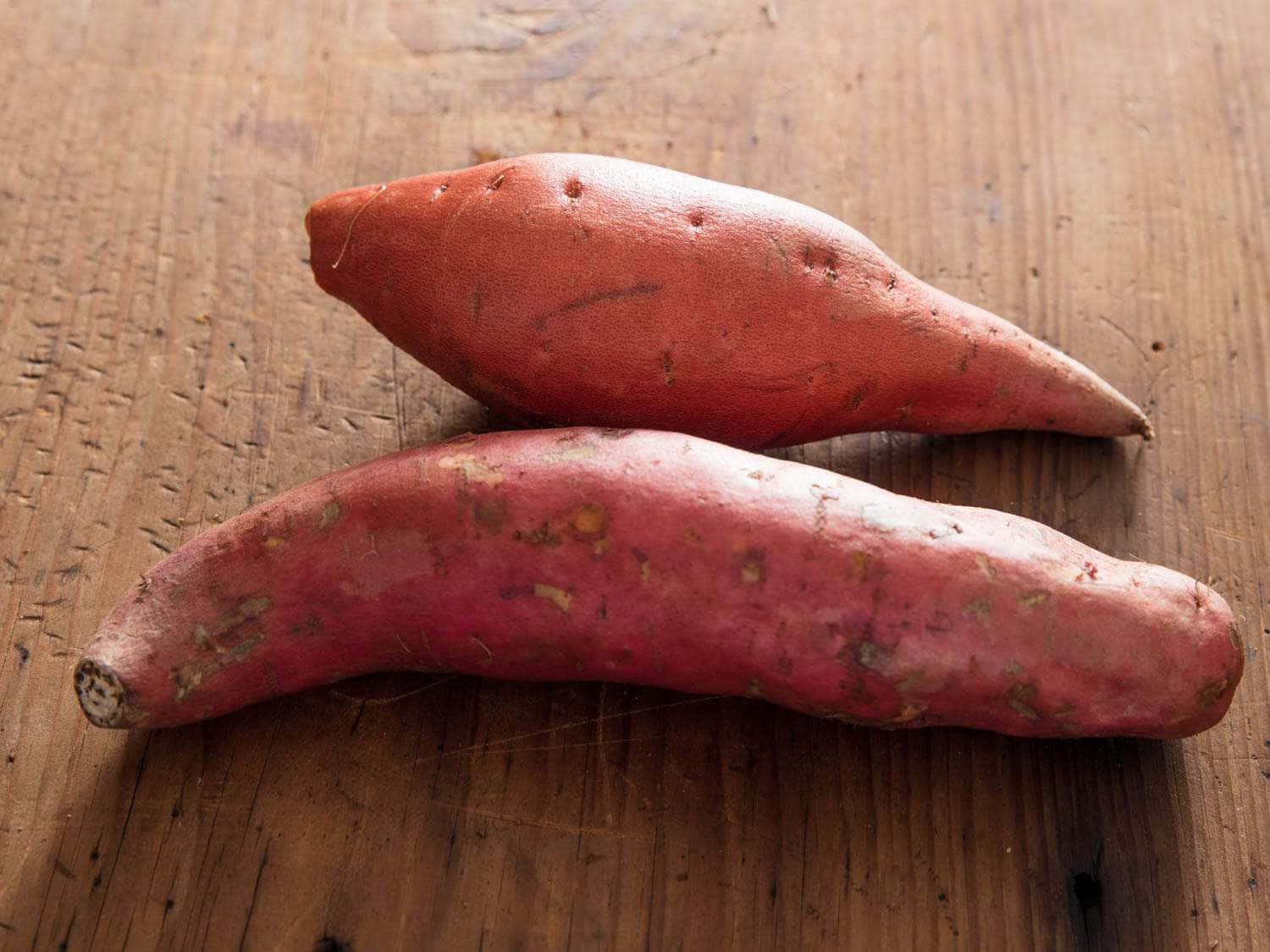 Red Potatoes 桌布 壁紙 — 兩個略帶紅色的番薯放在一塊經風化的木質表面上，表面帶有天然紋理和質感。