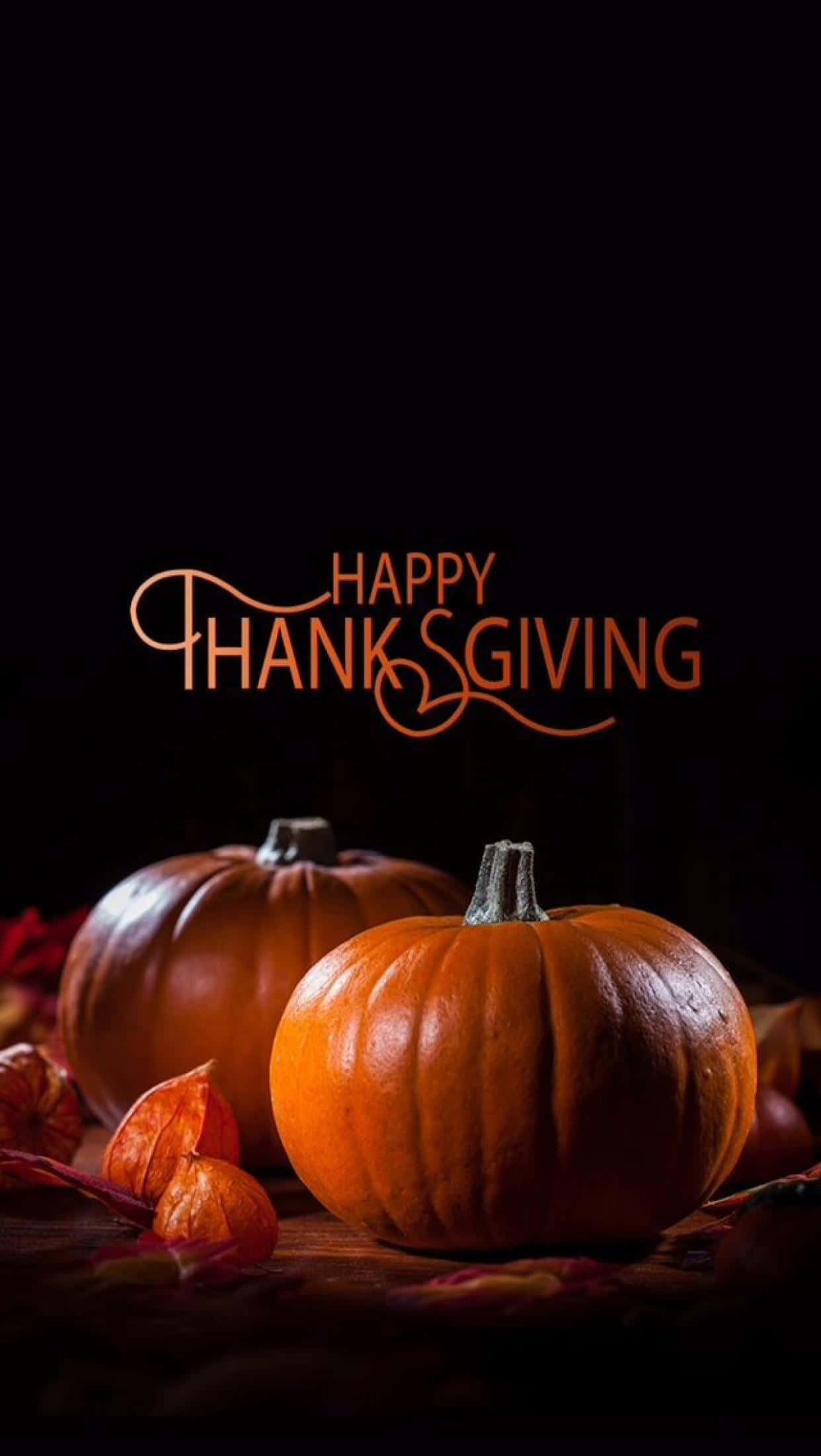Happy Thanksgiving 桌布 壁紙 — 兩個發光的南瓜放在深色木質表面上，旁邊有秋葉，在溫暖的燈光下，帶有「Happy Thanksgiving」文字。
