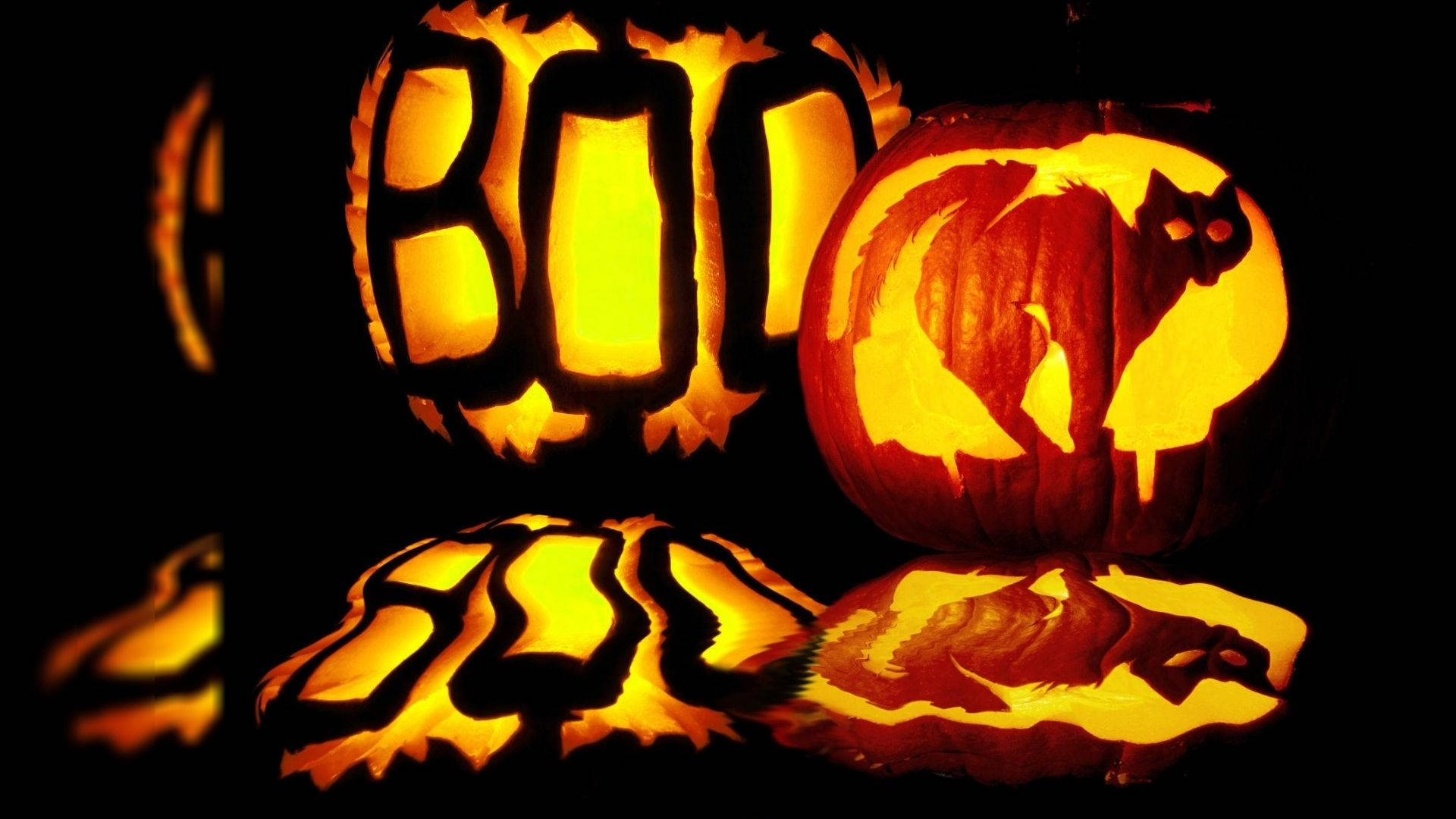 恐怖 桌布 壁紙 — 兩個發光的萬聖節南瓜，雕刻有「BOO」和貓剪影，在黑色背景的反射表面上投射溫暖的光線。