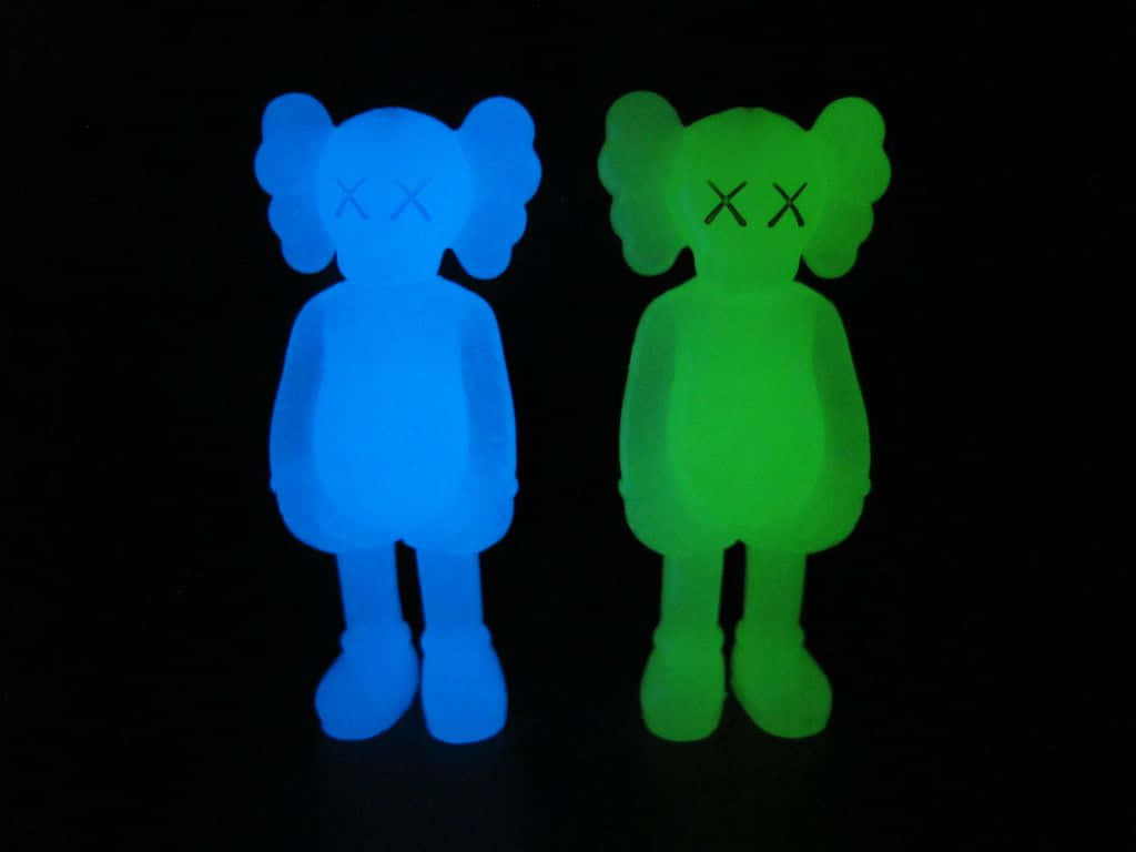 Kaws Astro Boy 桌布 壁紙 — 兩個發光的藍色和綠色KAWS人偶並排站在漆黑的背景前。
