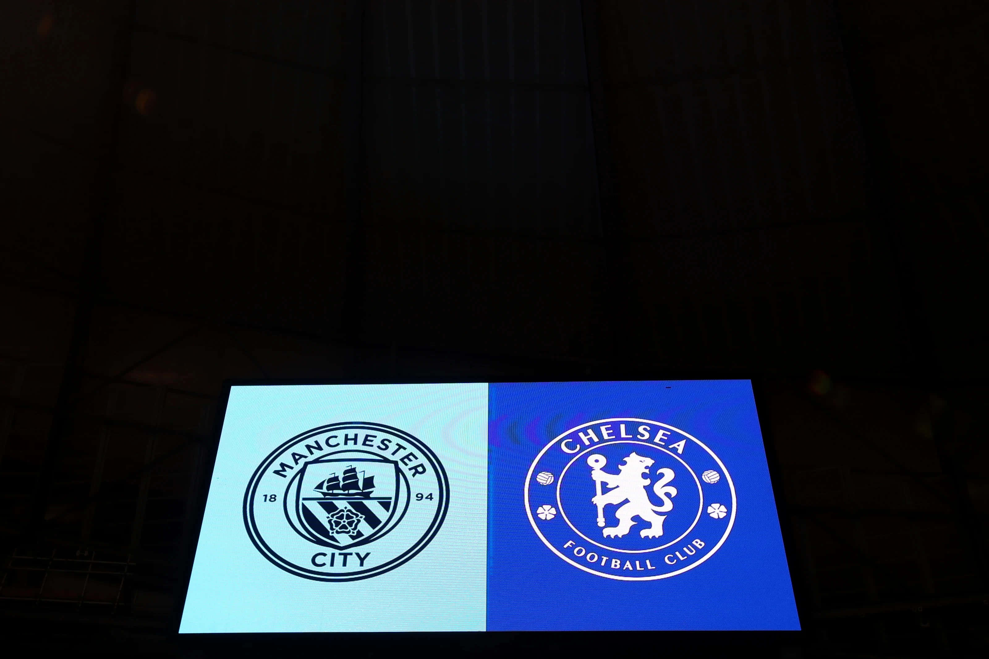 Chelsea 桌布 壁紙 — 兩個發光的足球會標誌曼城和車路士並排顯示在黑暗球場的屏幕上。
