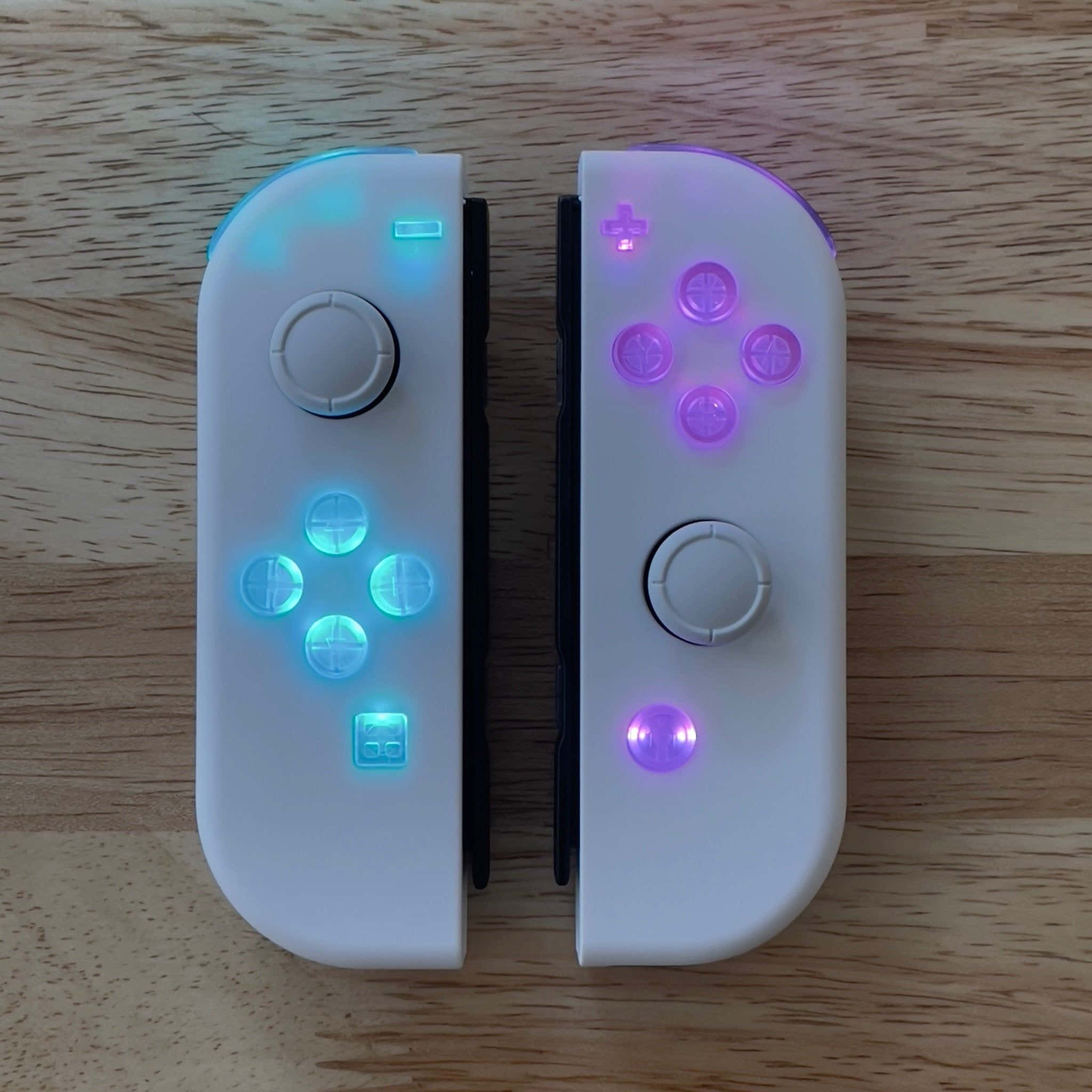 Gaming Accessories 桌布 壁紙 — 兩個白色Nintendo Switch Joy-Con在淺色木質表面上發出藍色和紫色的光芒。