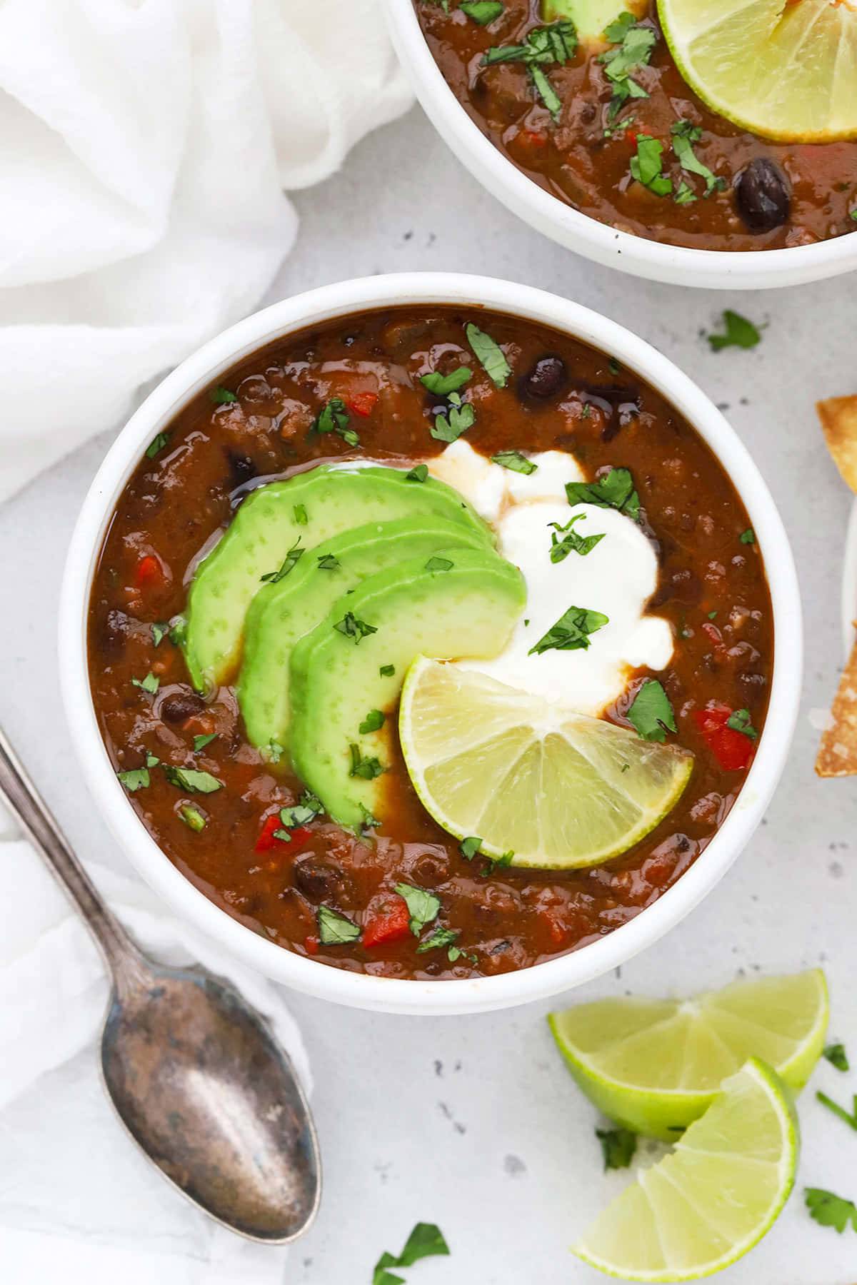 Black Bean Soup 桌布 壁紙 — 兩個碗裝著濃郁的深色辣椒，上面放著牛油果青檸醬和芫荽，放在淺灰色表面上。
