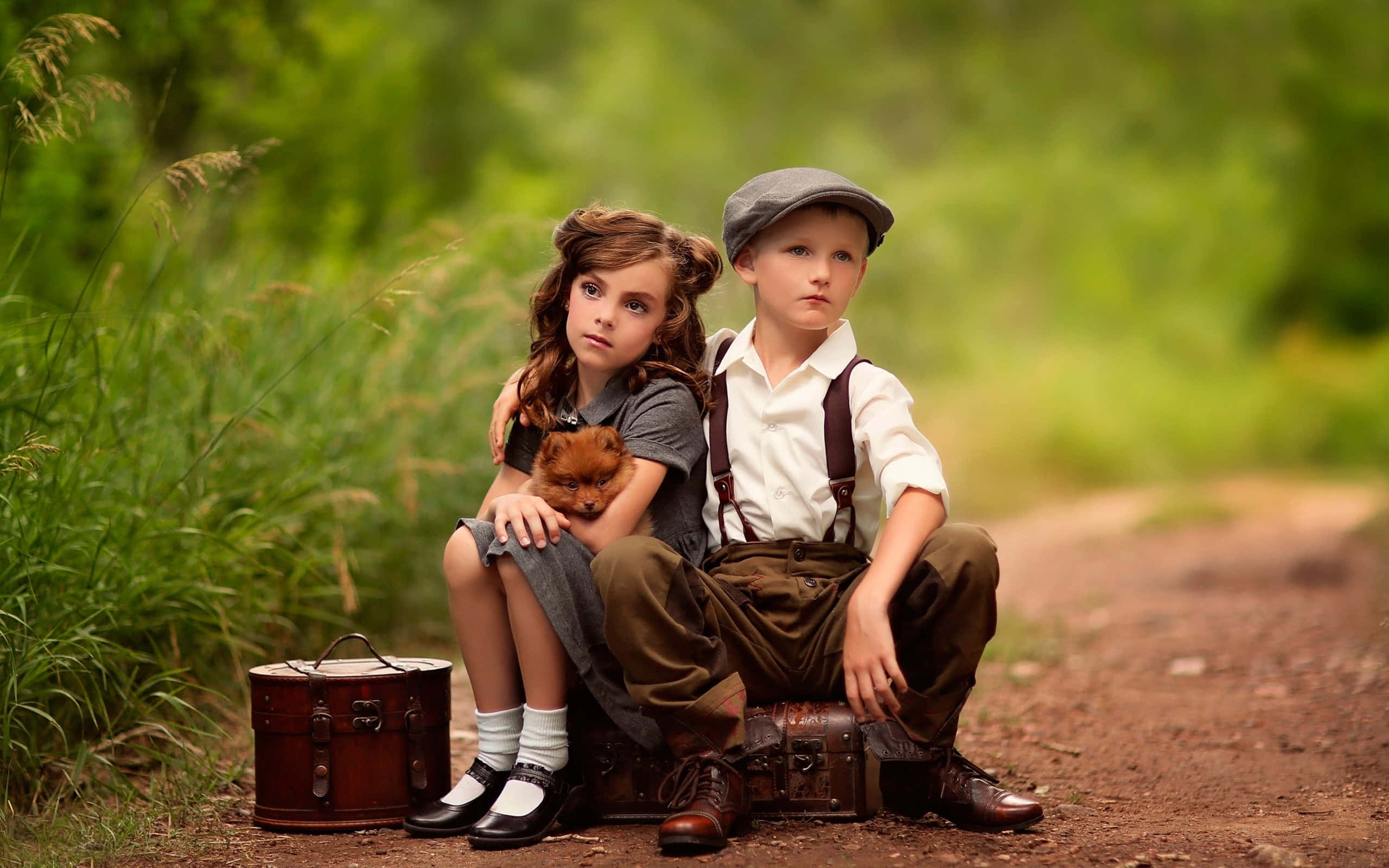 Cute Kids 桌布 壁紙 — 兩個穿著復古服裝的孩子坐在行李箱上，旁邊是一條泥濘小徑，身處茂密的綠色森林中，抱著一隻小狗。