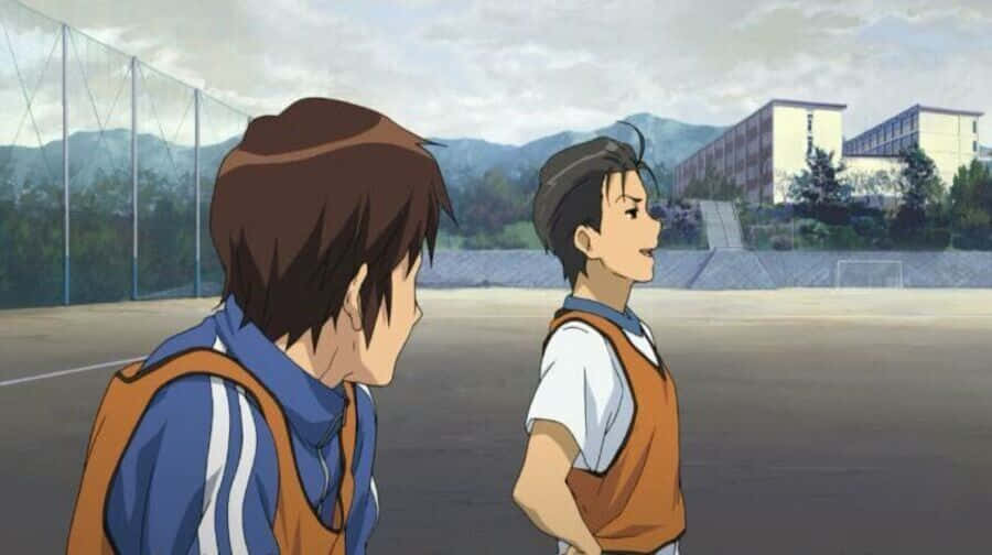Haruhi Taniguchi 桌布 壁紙 — 兩個穿著足球制服嘅動畫男仔喺學校球場傾偈，背景有山同建築物。