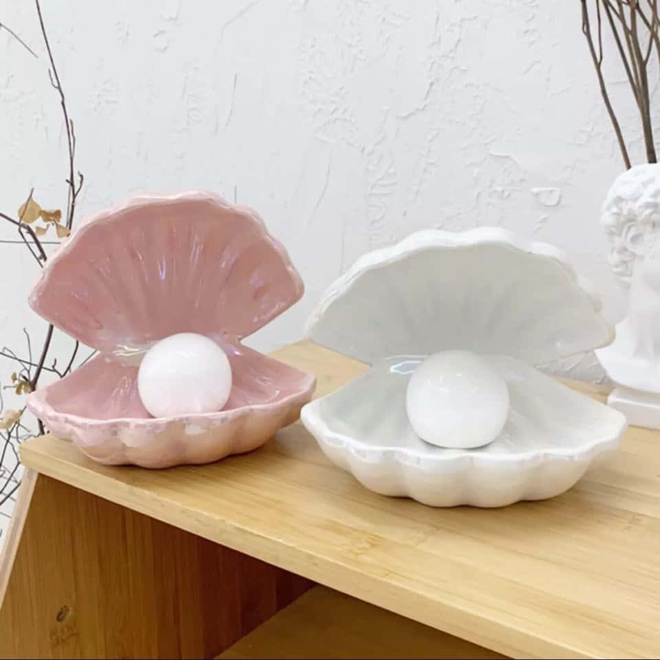 Clam Shell 桌布 壁紙 — 兩個粉紅色和白色的陶瓷貝殼碗，每個都托著一顆珍珠，放在木架上，旁邊有一個白色半身像和乾燥的樹枝。
