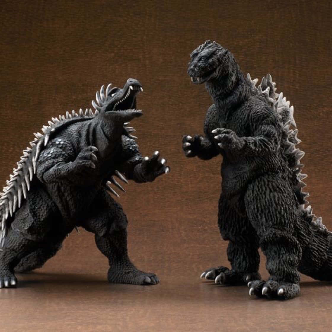 Godzilla Vs Anguirus 桌布 壁紙 — 兩個精細的哥斯拉動作人偶在純棕色背景前進行戲劇性的對峙。