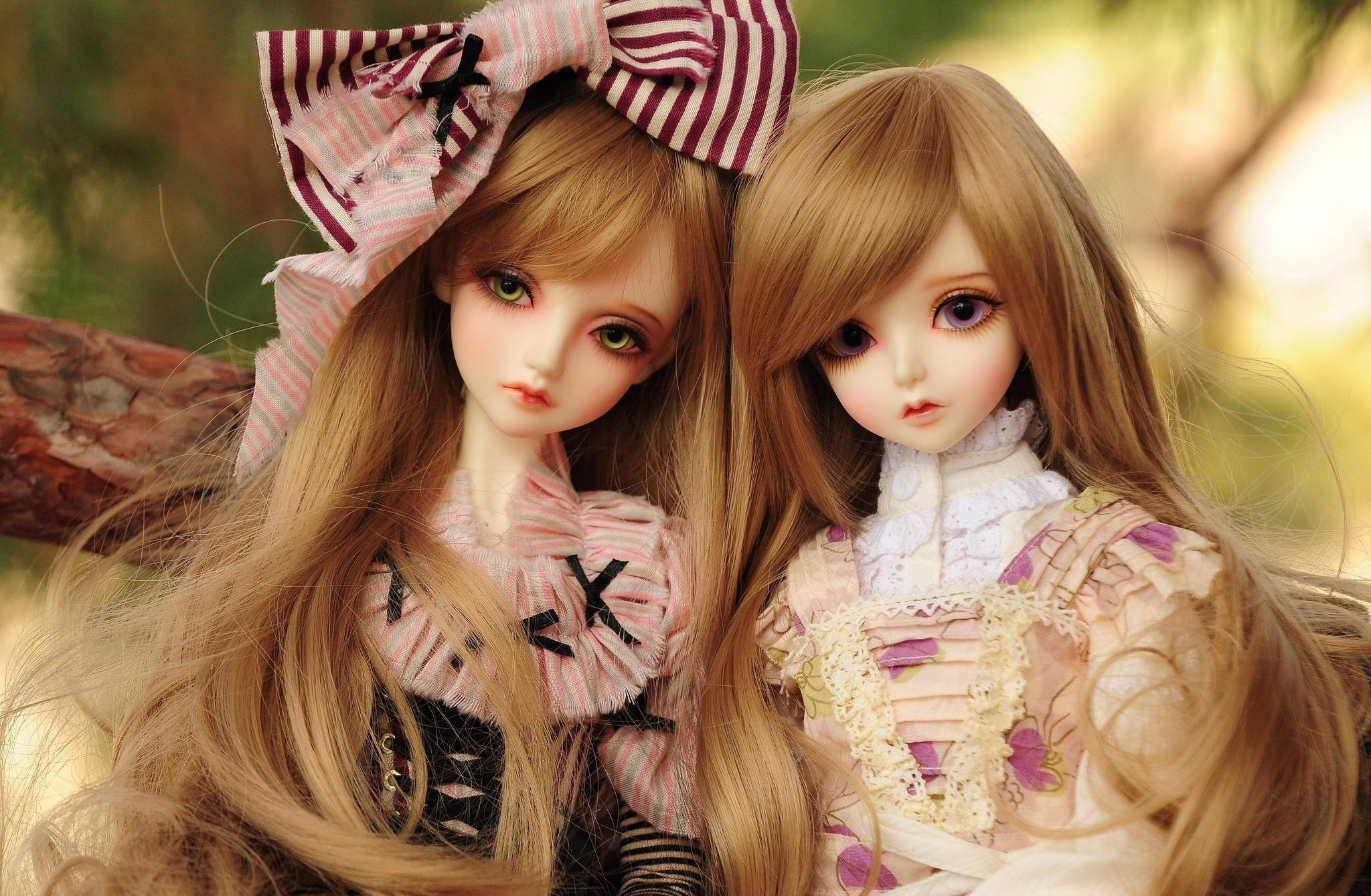 Doll 桌布 壁紙 — 兩個精緻的球體關節娃娃，擁有長長的金色頭髮和大而有表情的眼睛，在柔和的自然光下緊密地坐在戶外。