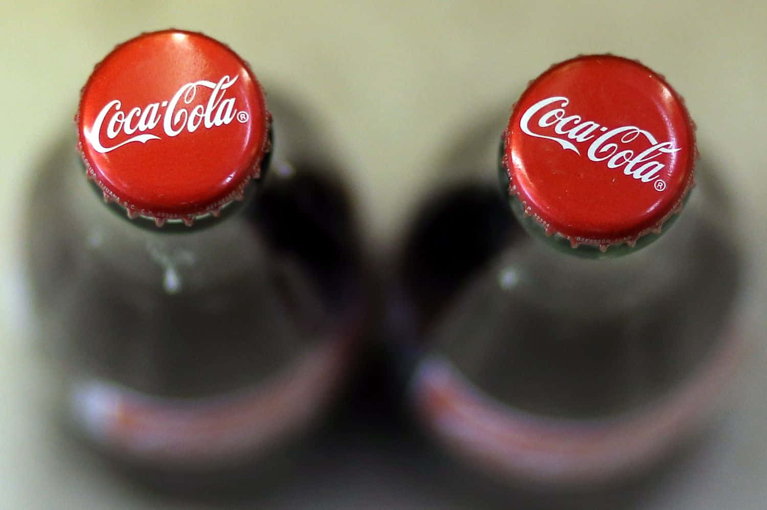 coca cola 桌布 壁紙 — 兩個紅色蓋的玻璃可口可樂瓶，淺景深，背景為柔和米色。