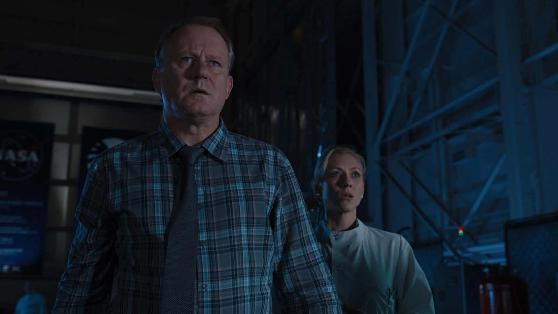 Erik Selvig 桌布 壁紙 — 兩個緊張的人物在昏暗藍色照明的NASA設施中，帶著警覺的表情向上凝視。