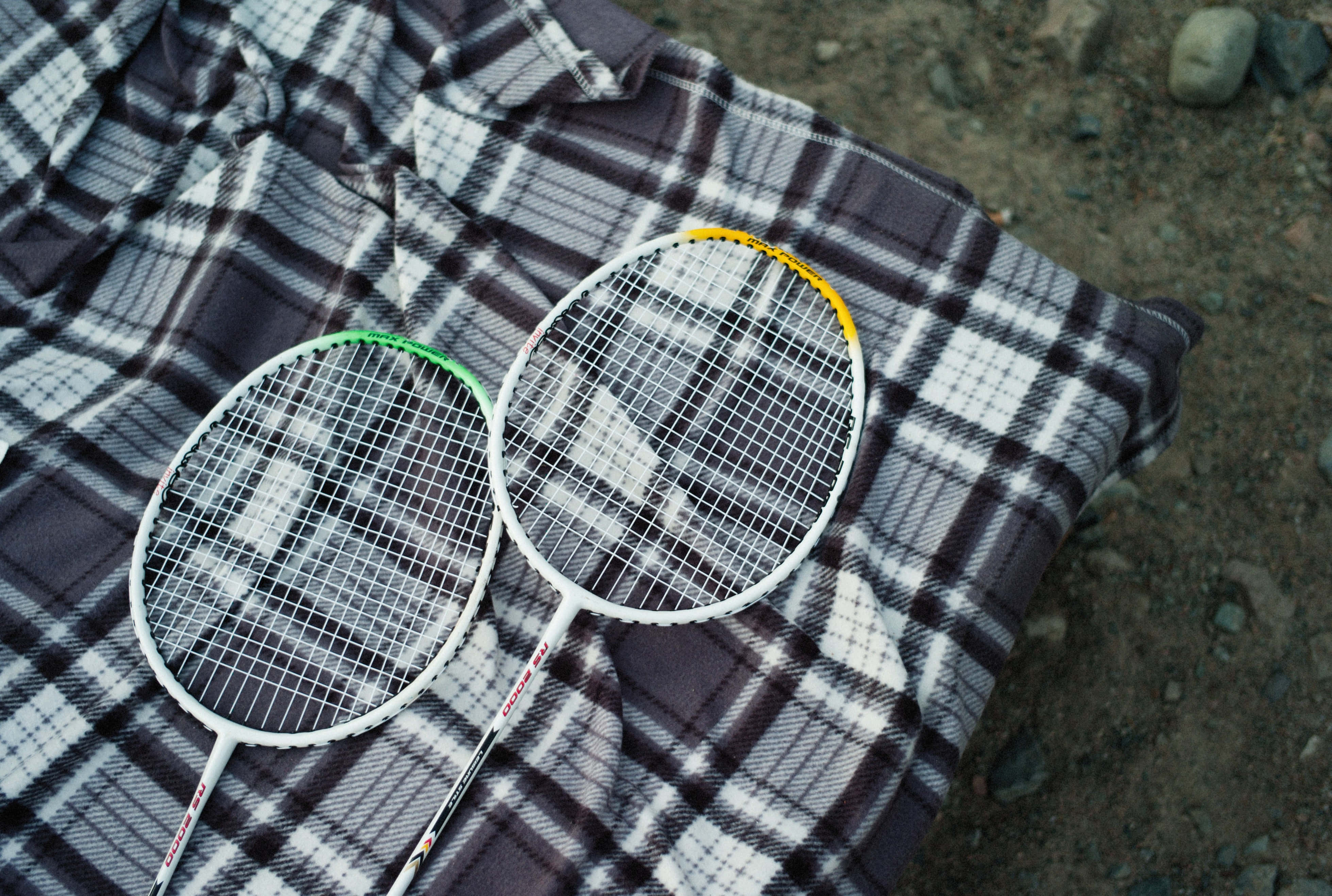Badminton 桌布 壁紙 — 兩個羽毛球拍放在鋪在碎石地上的格仔毯上。
