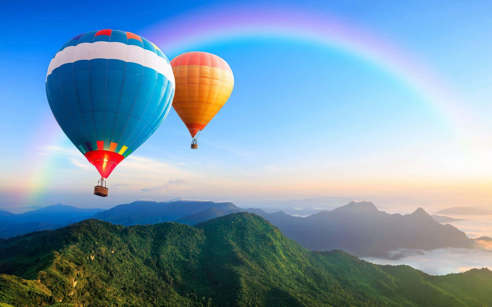 Hot Air Balloon 桌布 壁紙 — 兩個色彩繽紛的熱氣球在鬱鬱蔥蔥的綠色山脈上空翱翔，一道鮮豔的彩虹橫跨清澈的藍天。