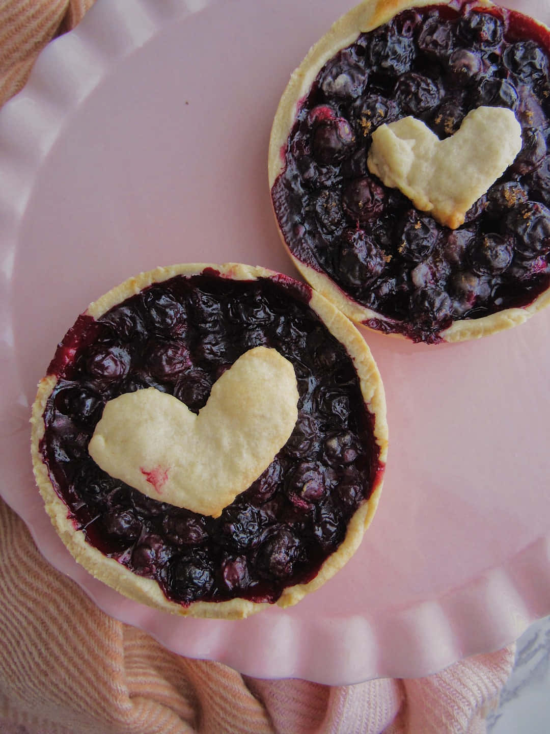Blueberries Tart 桌布 壁紙 — 兩個藍莓批，上面有心形酥皮，放在粉紅色碟上，碟下墊著桃色布。