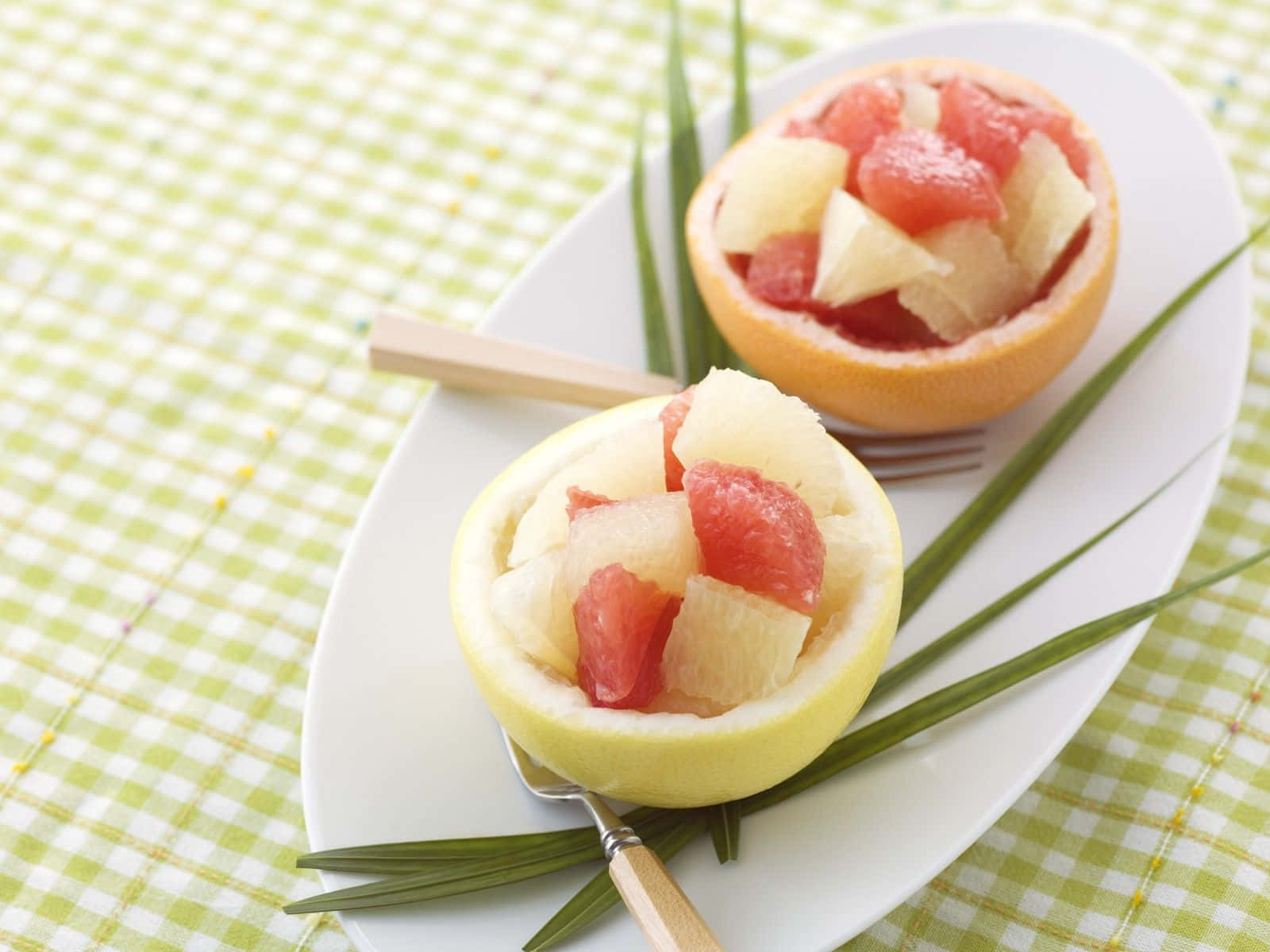 Spring Desserts 桌布 壁紙 — 兩個西柚半邊，裝滿粉紅西柚和菠蘿塊，放在白色碟上，配上綠葉，置於格仔枱布上。