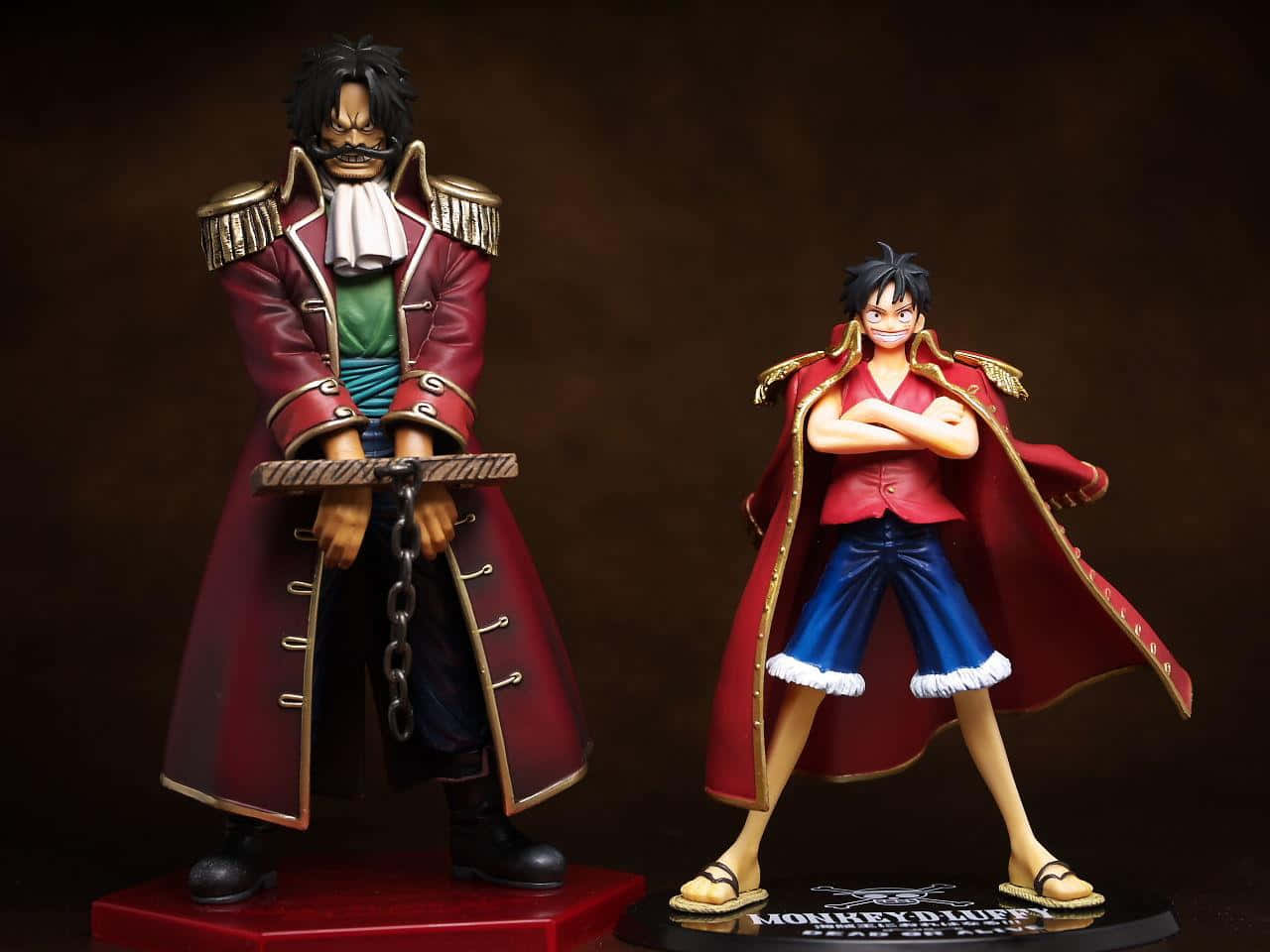 King Of The Pirates 桌布 壁紙 — 兩個詳細的動漫人物模型，分別是蒙奇·D·路飛和他的成年版本，自信地站在深棕色背景前。