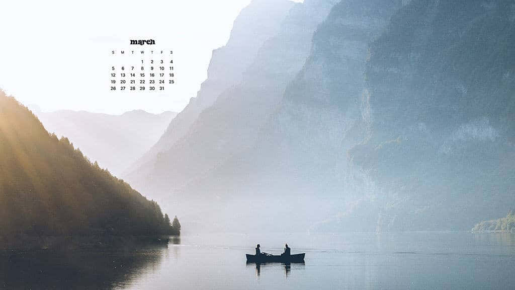 March Desktop 桌布 壁紙 — 兩個身影在煙霧瀰漫的山間湖上划著小船，柔和的晨光穿過高聳的山峰。