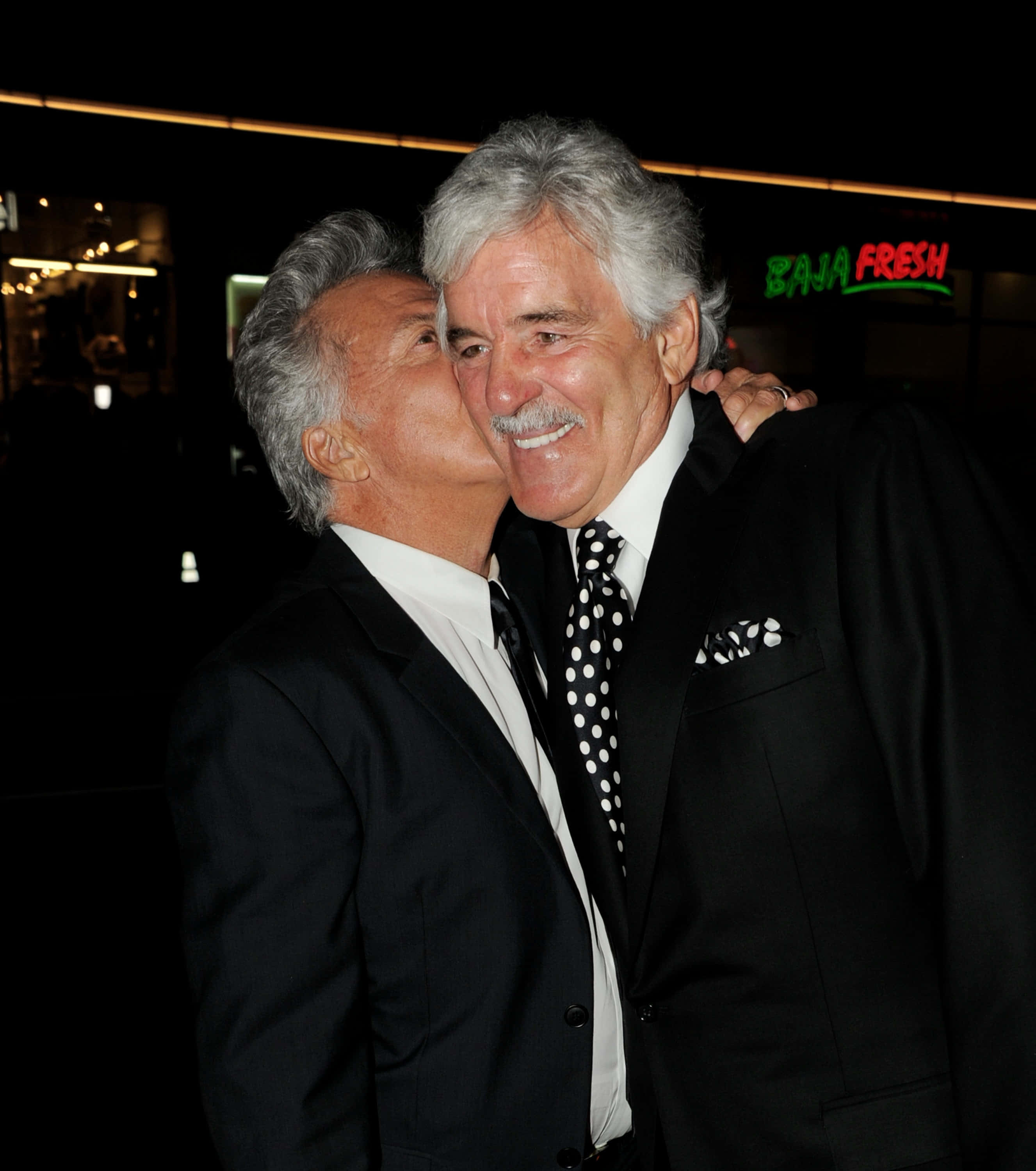 Dennis Farina 桌布 壁紙 — 兩個身穿黑色西裝的男人在夜晚的霓虹燈下熱情擁抱，身後有「Baja Fresh」的招牌閃爍。