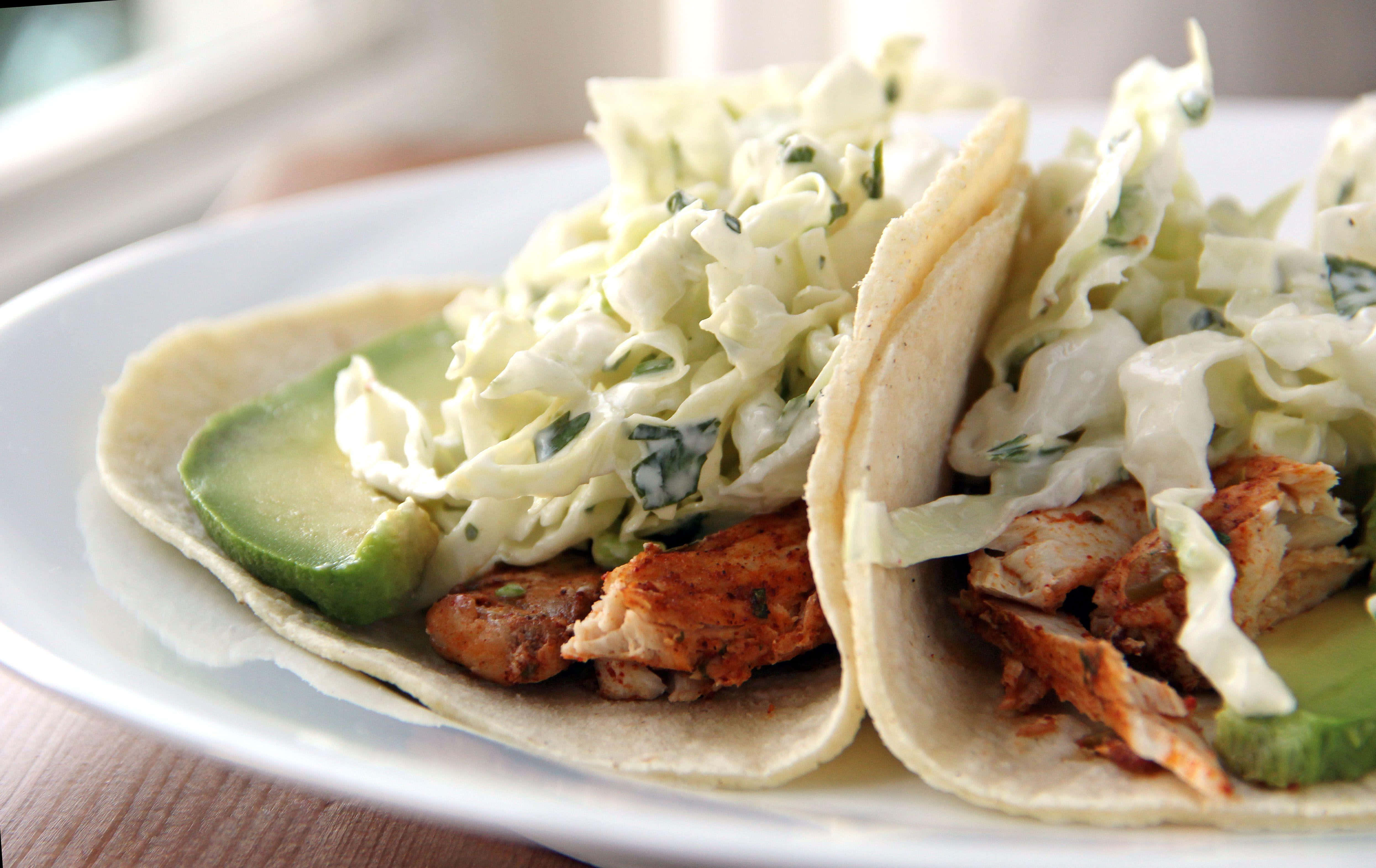 Taco 桌布 壁紙 — 兩個軟玉米餅，內餡有雞絲、牛油果和椰菜沙律，放在白色碟上，背景是木桌。