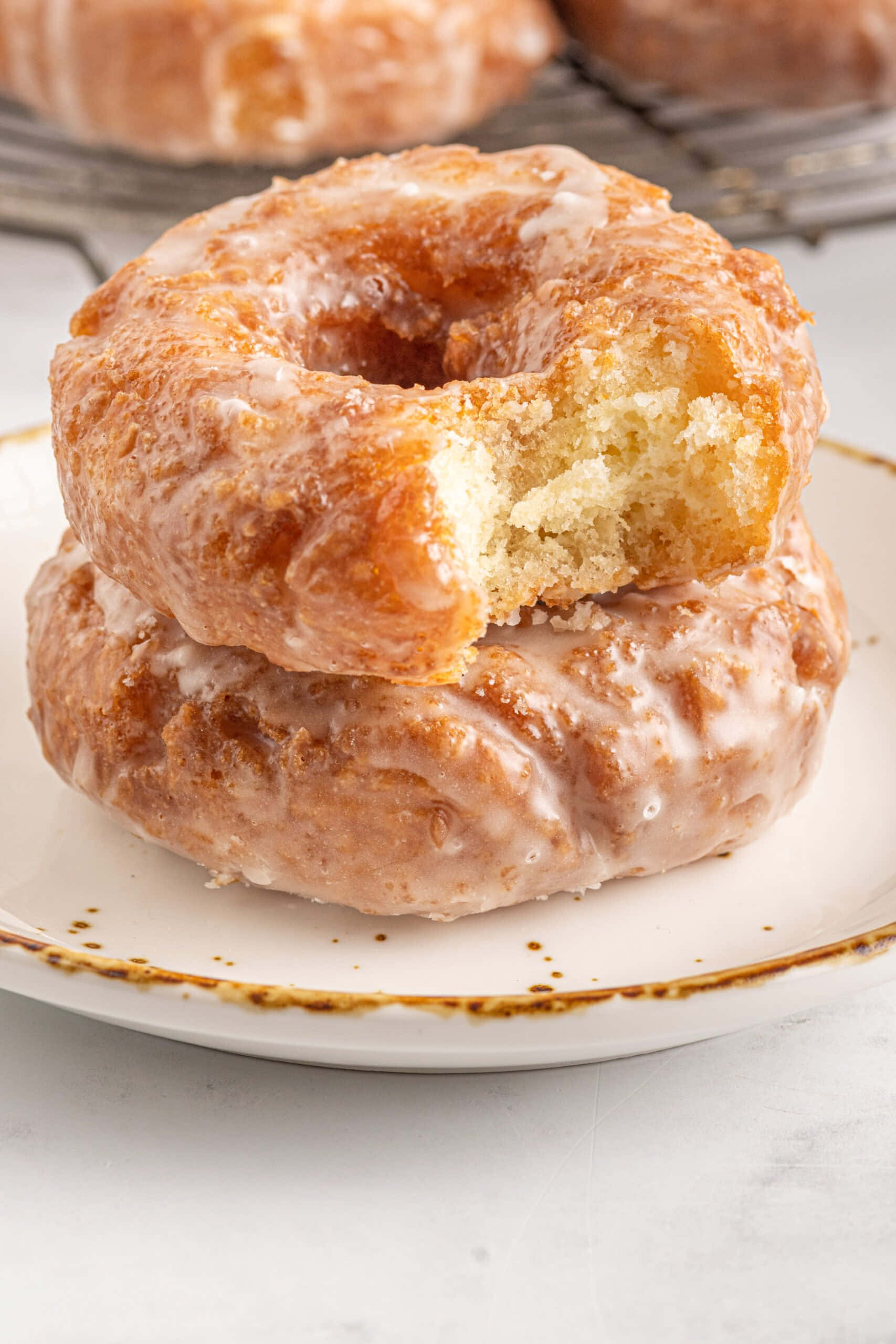 Glazed Donut 桌布 壁紙 — 兩個釉面冬甩疊在碟上，其中一個被咬了一口，露出軟綿綿的內部。