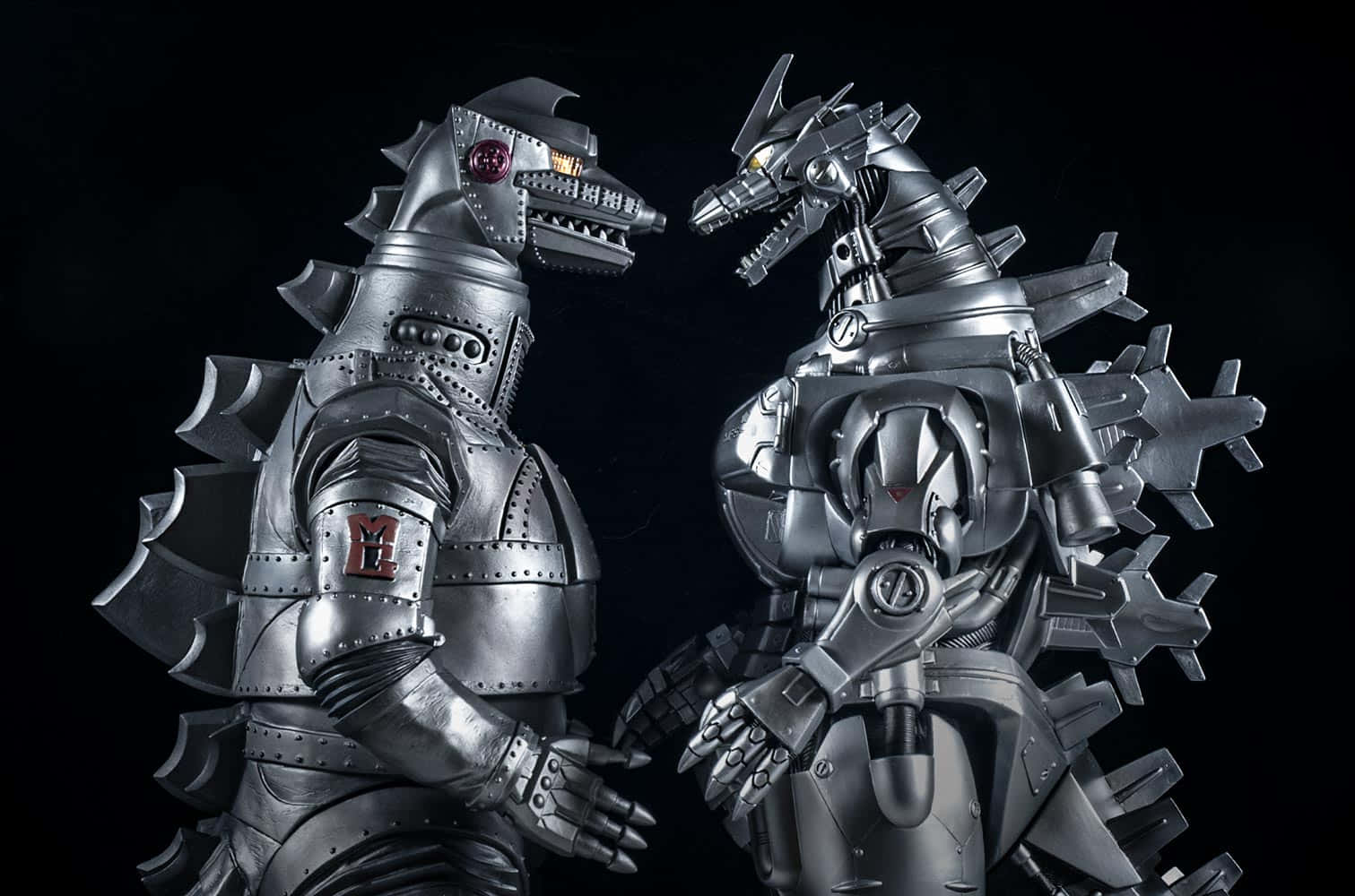 Robot Godzilla 桌布 壁紙 — 兩個金屬製的哥斯拉和王者基多拉雕像在黑色背景前進行戲劇性的攝影棚拍攝。
