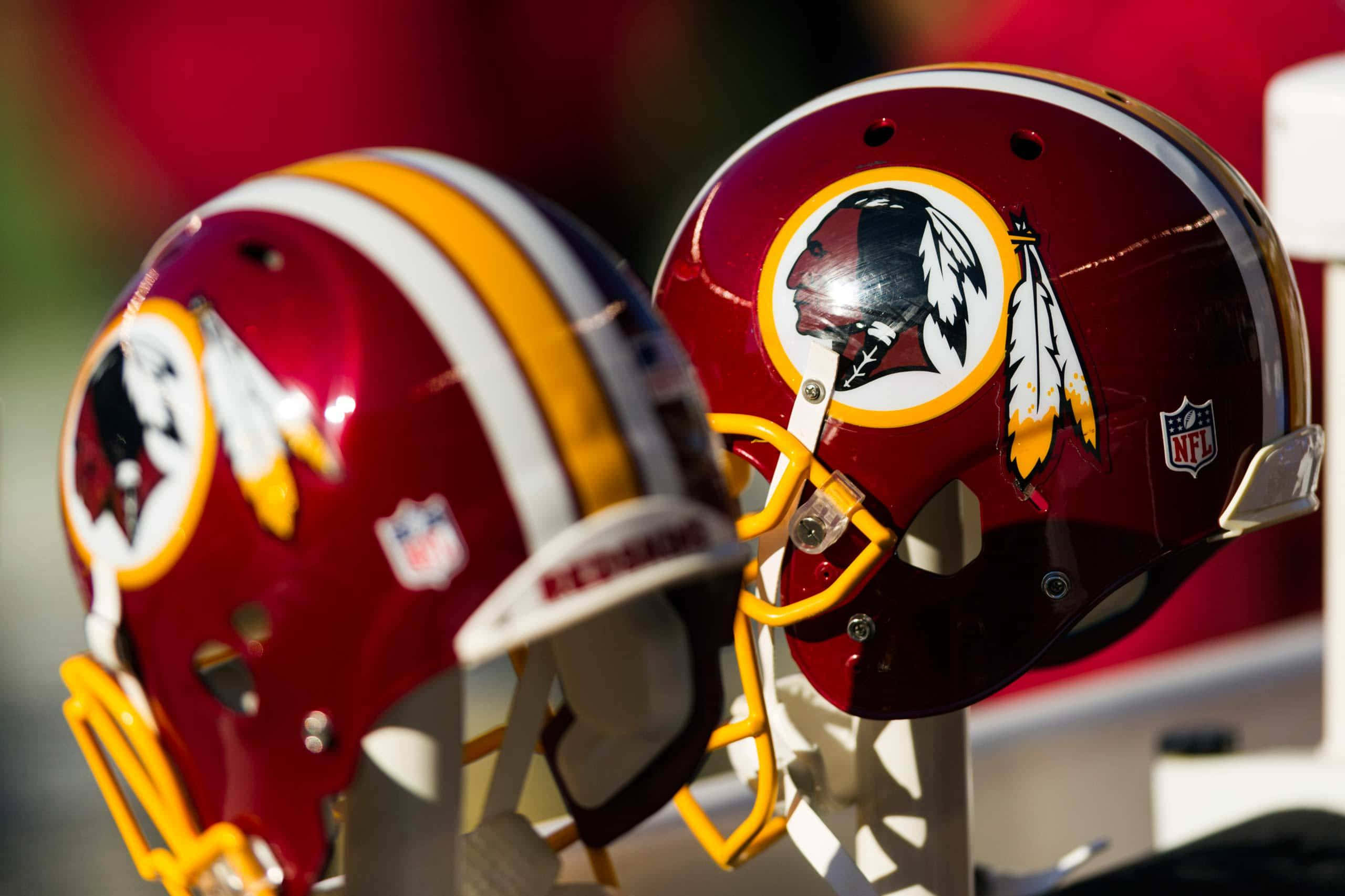 Washington Football 桌布 壁紙 — 兩個閃亮的酒紅色華盛頓美式足球隊頭盔，帶有金色和白色點綴，並排放在明亮的陽光下。