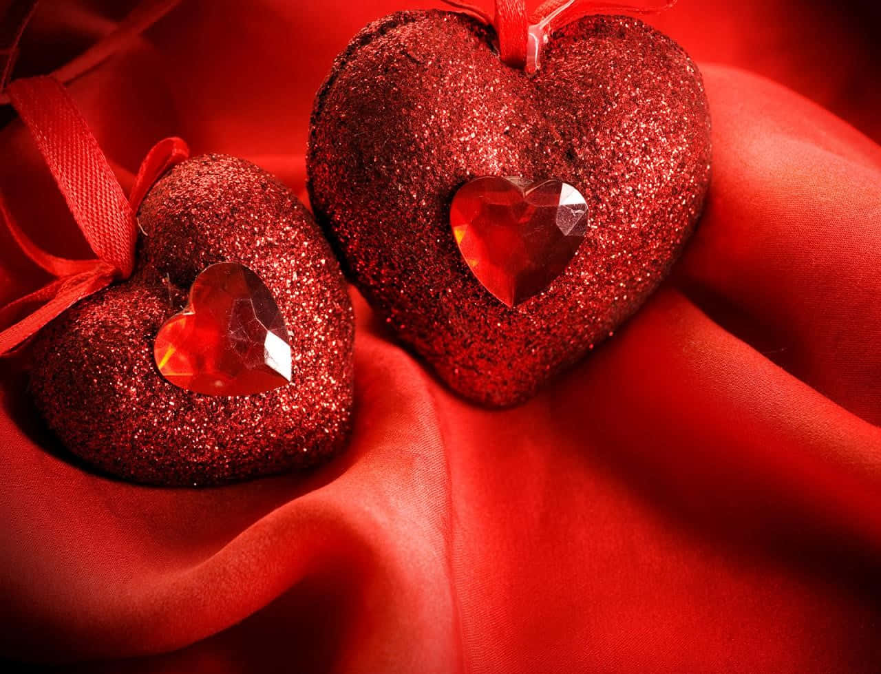 Red Heart 桌布 壁紙 — 兩個閃閃發光的紅色心形裝飾品，內部有水晶心，放置在濃郁的紅色緞面上。