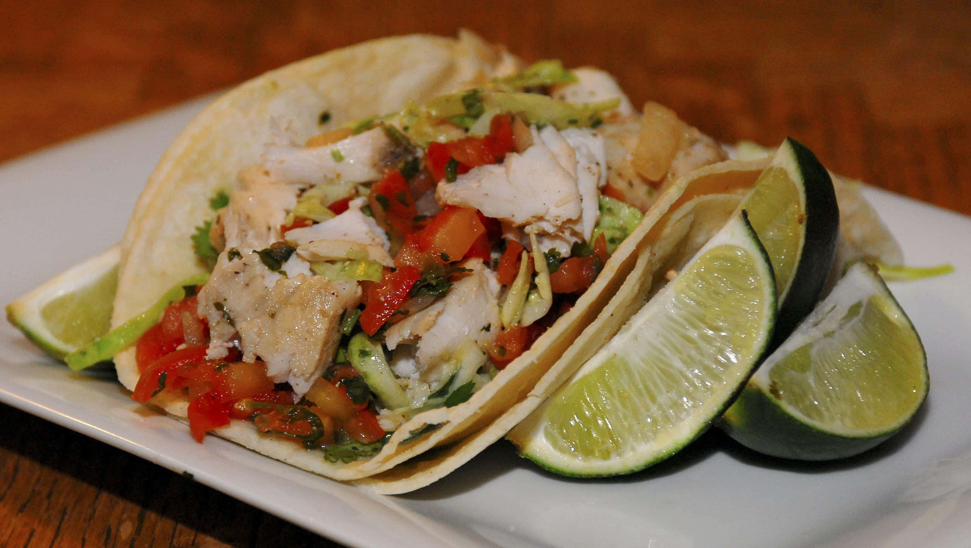 Taco 桌布 壁紙 — 兩個魚肉墨西哥卷，上面放上新鮮的pico de gallo和牛油果，放在白色碟子上，配上青檸角，置於木桌上。