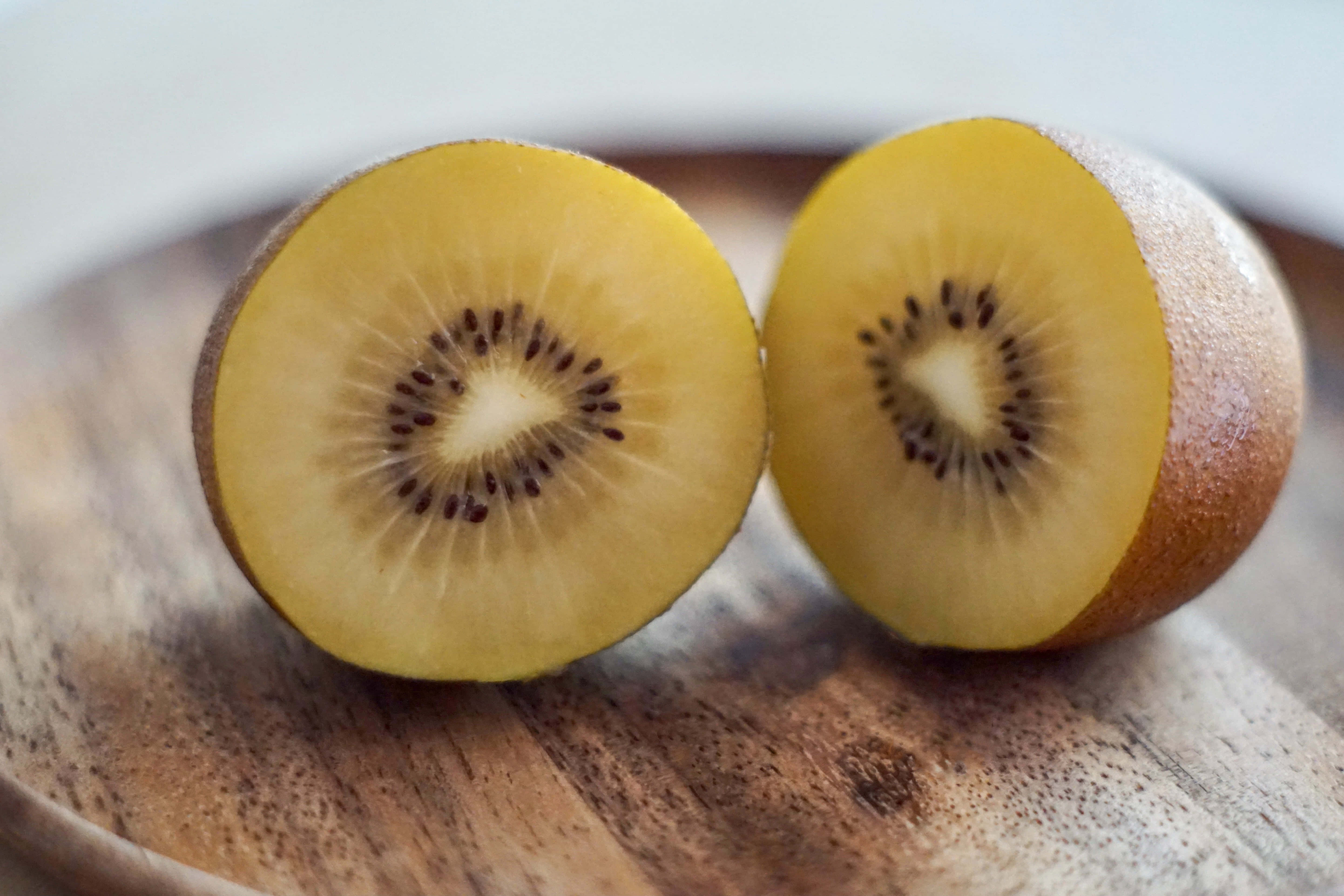 Kiwi 桌布 壁紙 — 兩個黃金奇異果切開一半，露出鮮黃色的果肉和黑色種子，放在一個質樸的木盤上。