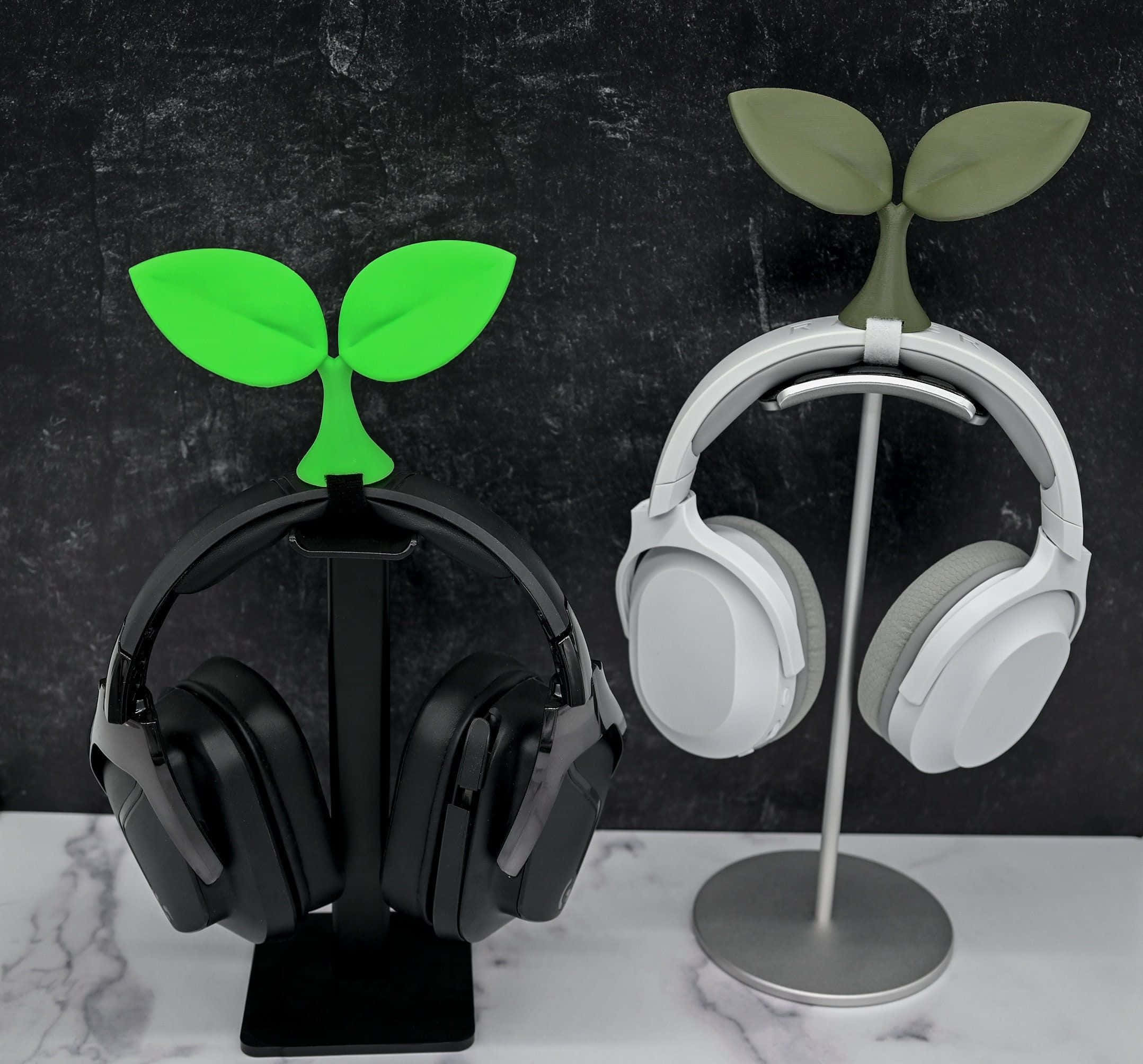 Gaming Accessories 桌布 壁紙 — 兩個黑色和白色的耳機放在植物形狀的支架上，靠在深色紋理牆上，置於大理石表面。