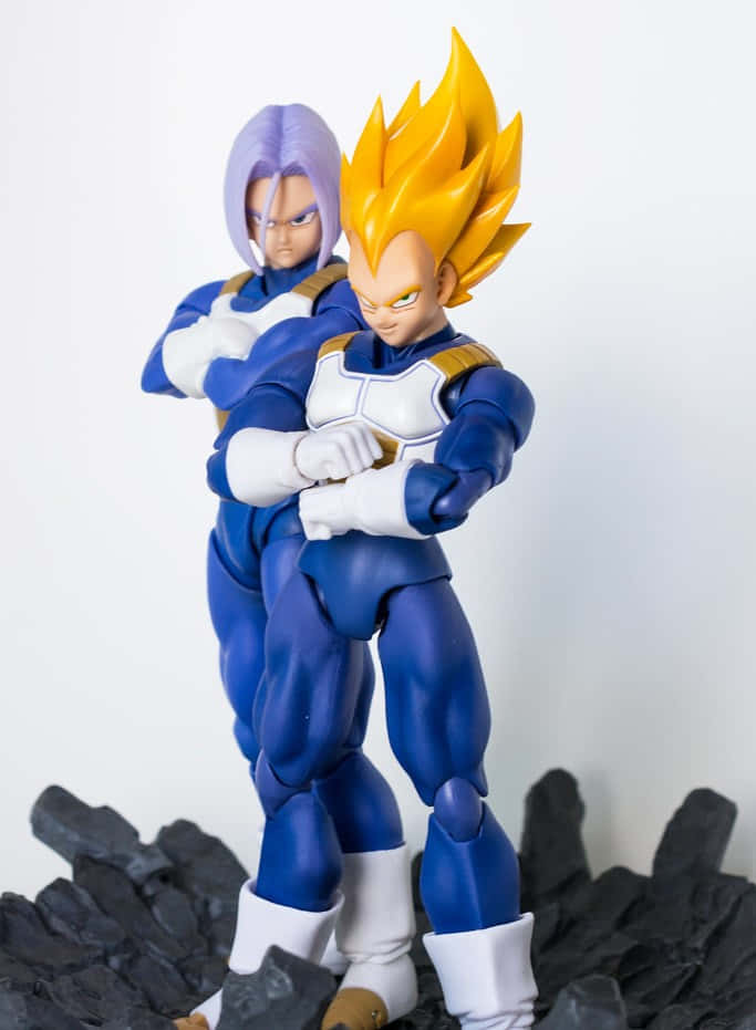 Vegeta And Trunks 桌布 壁紙 — 兩個龍珠動作人偶，一個有紫色頭髮，另一個有尖刺黃色頭髮，在白色背景的黑色岩石上擺姿勢。