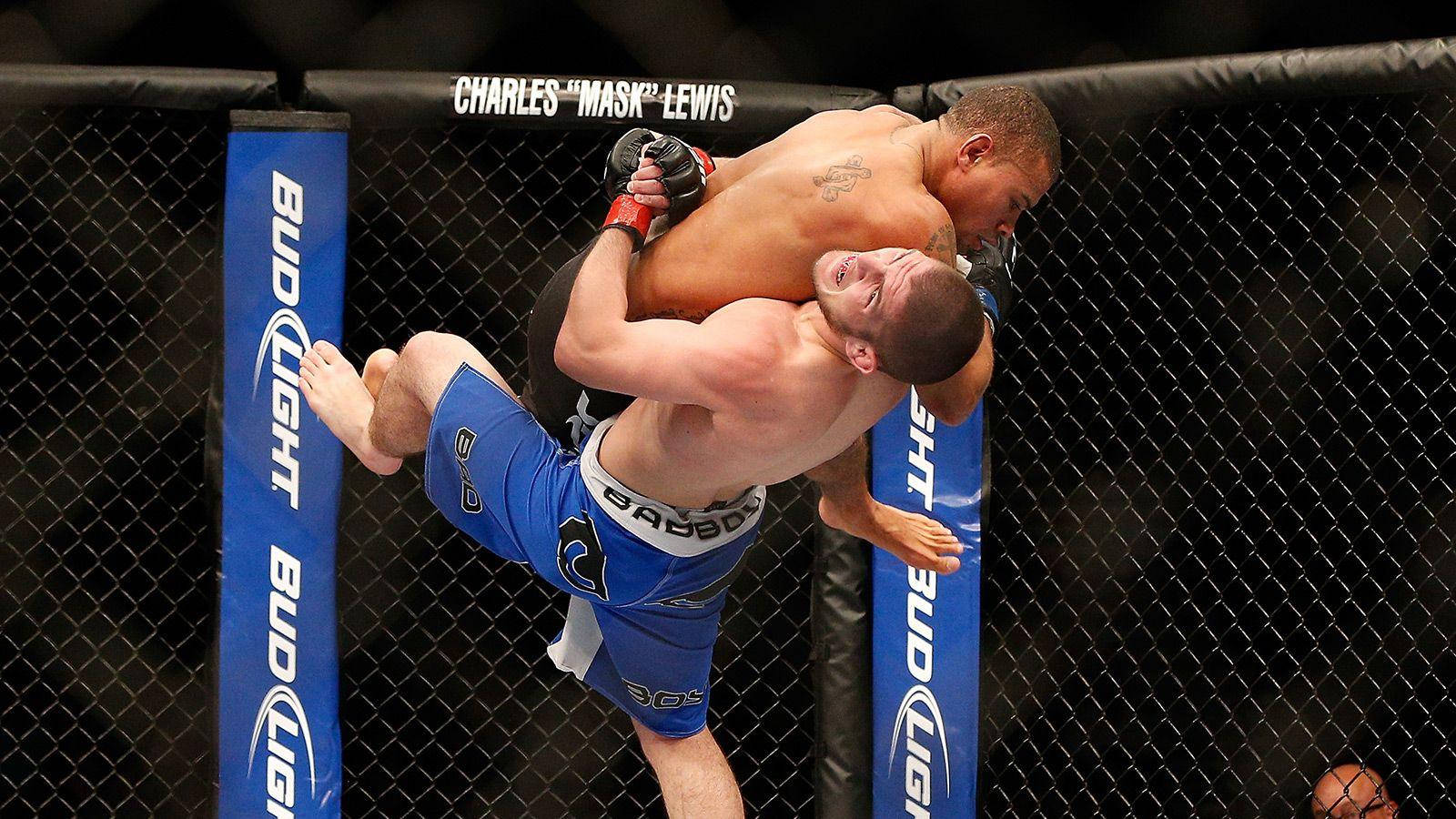 UFC 桌布 壁紙 — 兩名MMA拳手在籠內激烈纏鬥，其中一人對著圍欄執行強力摔倒。
