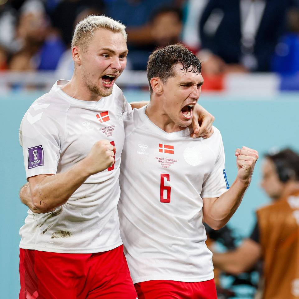 Denmark 桌布 壁紙 — 兩名丹麥足球運動員身穿白色球衣和紅色短褲，在球場上緊握拳頭、張開嘴巴熱情慶祝。