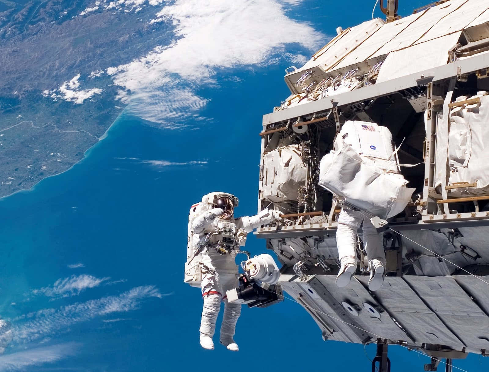 Space Exploration 桌布 壁紙 — 兩名太空人漂浮在國際太空站外，背景是地球充滿活力的藍色海洋和白色雲層。