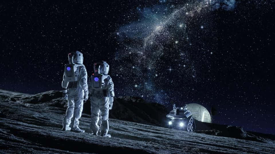 Space Colonization 桌布 壁紙 — 兩名太空人站在岩石外星月球上，凝視著充滿活力的星場，附近有漫遊車和圓頂棲息地。