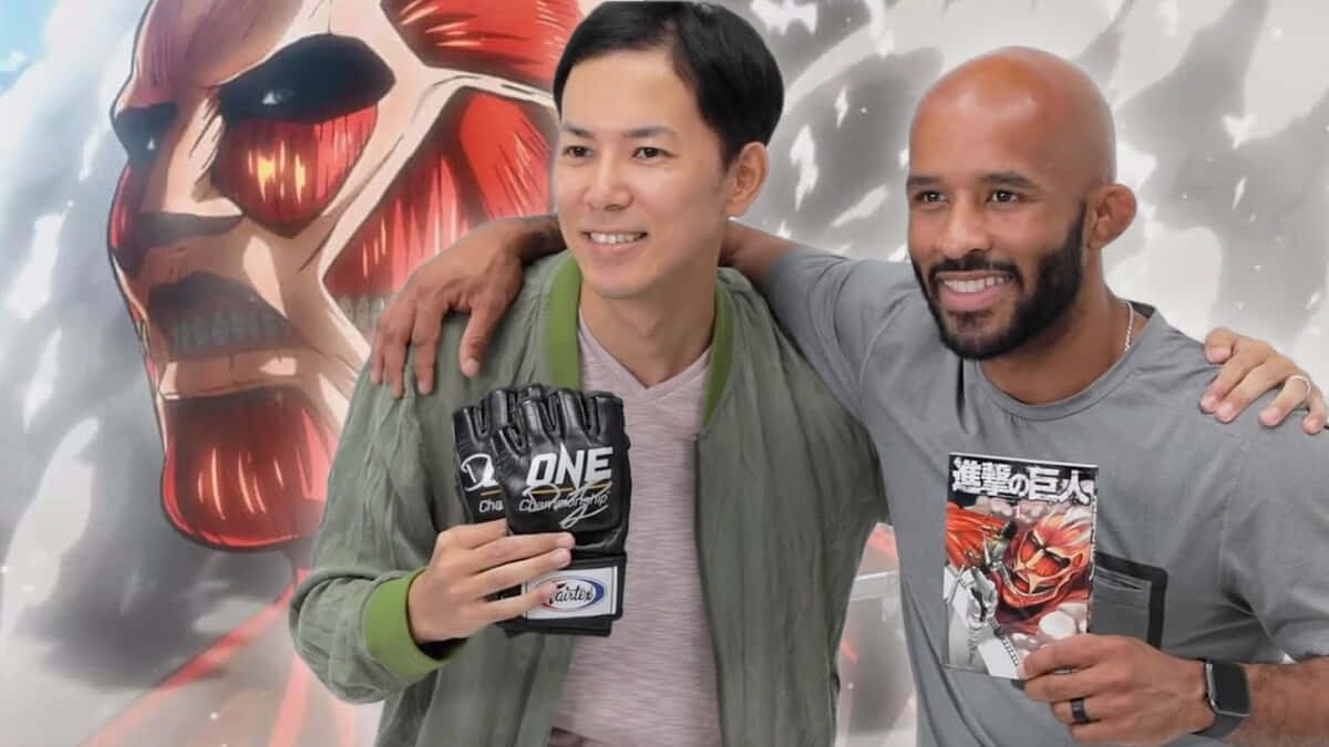 Isayama Hajime 桌布 壁紙 — 兩名微笑男子手持ONE Championship手套及進擊的巨人周邊商品，在巨型巨人壁畫前擺姿勢。