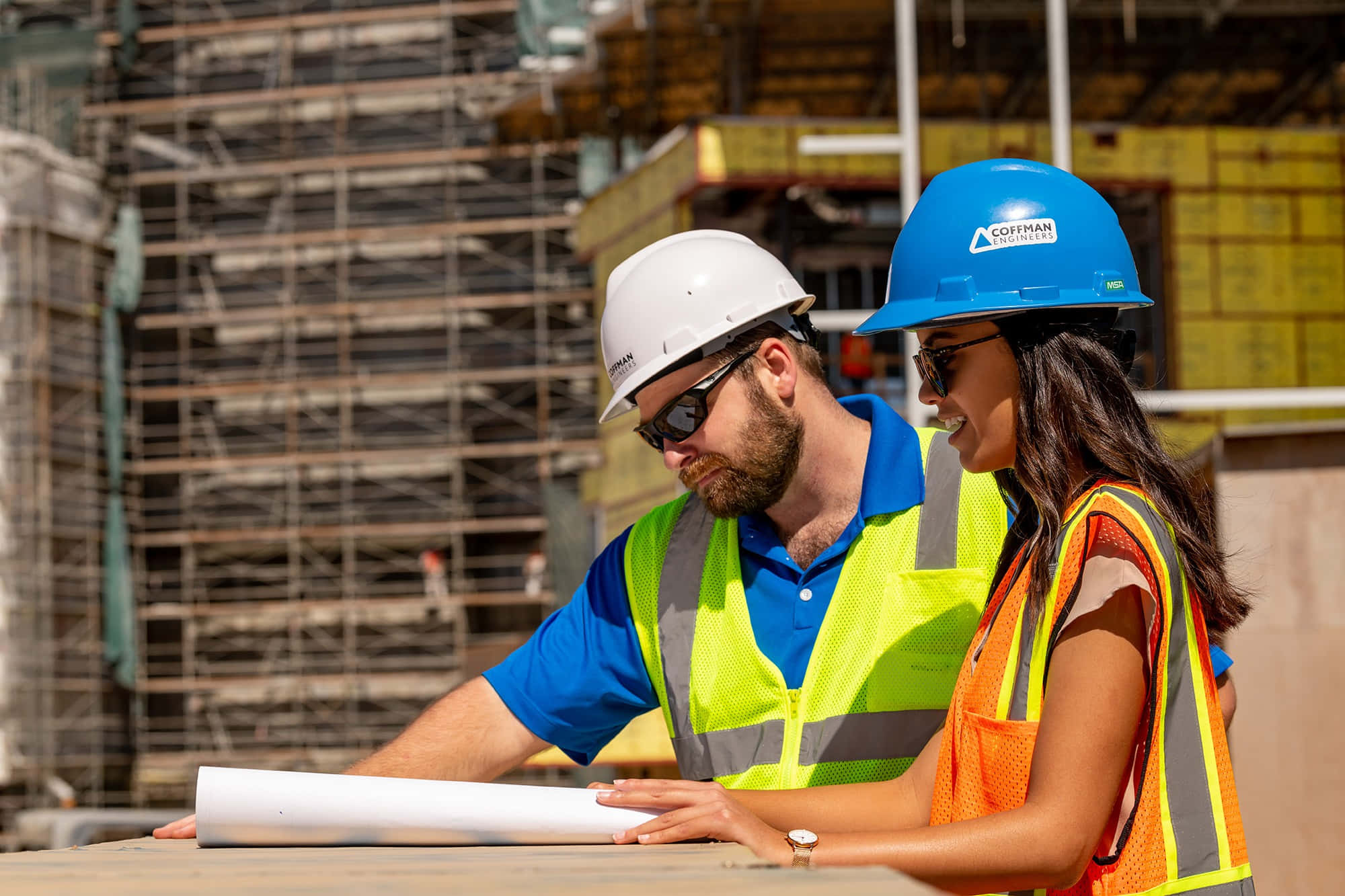 Engineer 桌布 壁紙 — 兩名戴著安全帽和穿著安全背心的建築工人在繁忙的建築工地上，在明亮的陽光下審閱藍圖。
