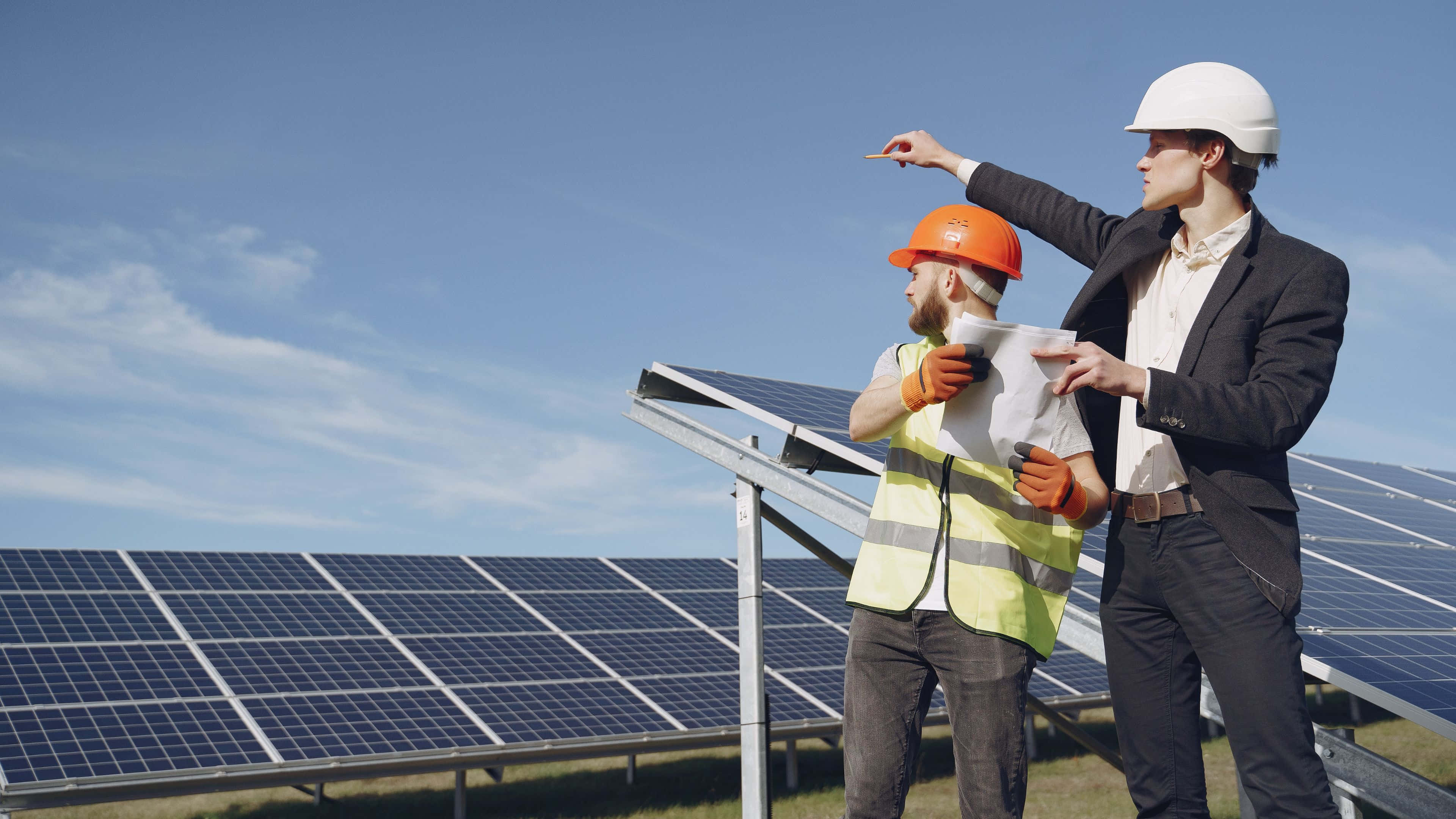 Solar Panel 桌布 壁紙 — 兩名戴著安全帽的工程師在晴朗的天空下審視藍色太陽能板。