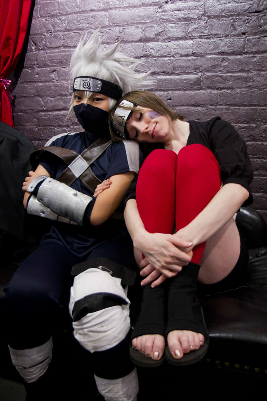 Kakashi And Rin 桌布 壁紙 — 兩名扮演火影忍者角色的Cosplayer緊貼著坐在磚牆前的皮梳化上，一人將頭靠在另一人的肩膀上。