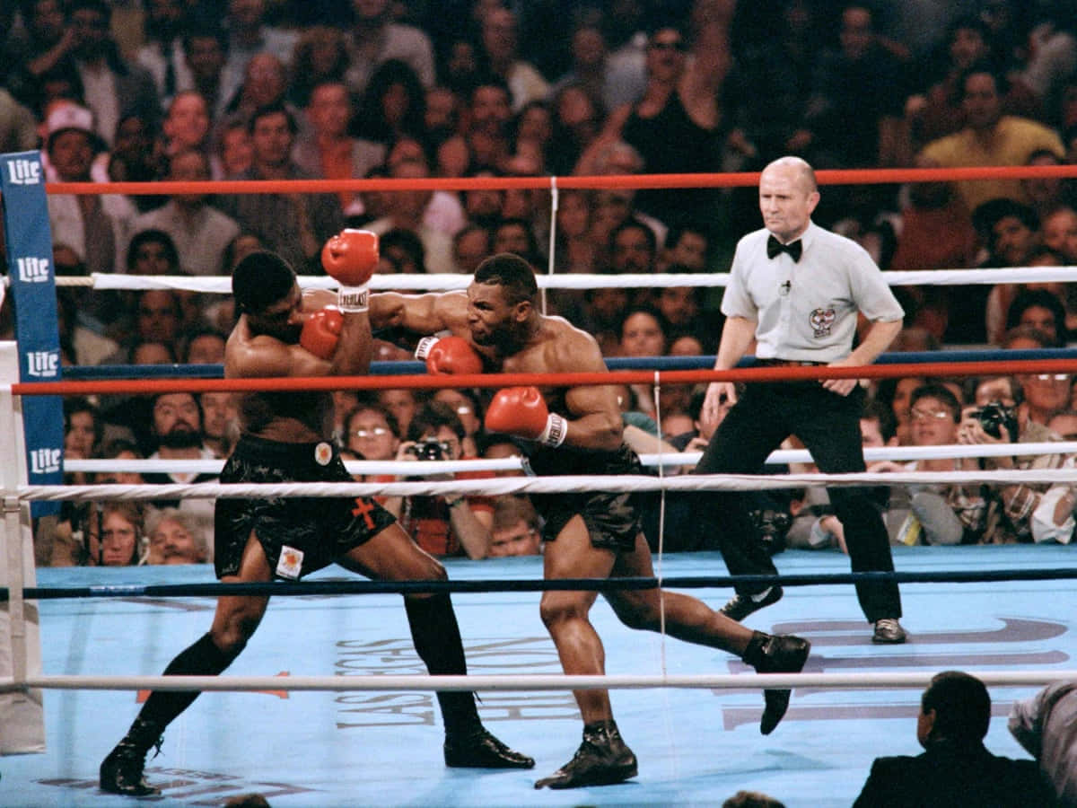 mike tyson 桌布 壁紙 — 兩名拳擊手在明亮的燈光下於擂台上交鋒，裁判在旁觀看，全場觀眾歡呼。