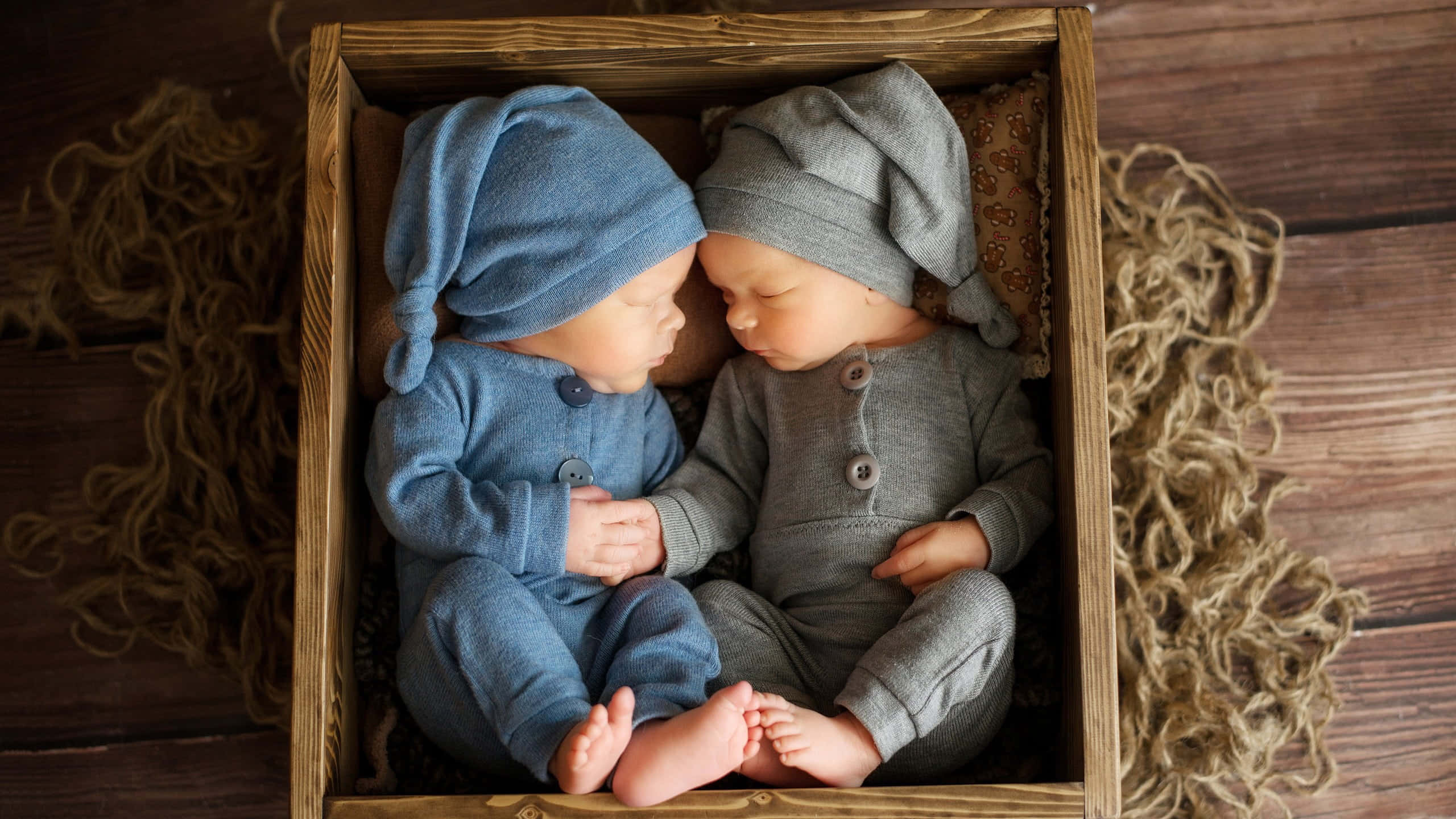 Cute Babies 桌布 壁紙 — 兩名新生雙胞胎在木箱中安睡，身穿柔軟的藍色和灰色針織套裝，他們的小腳互相觸碰。