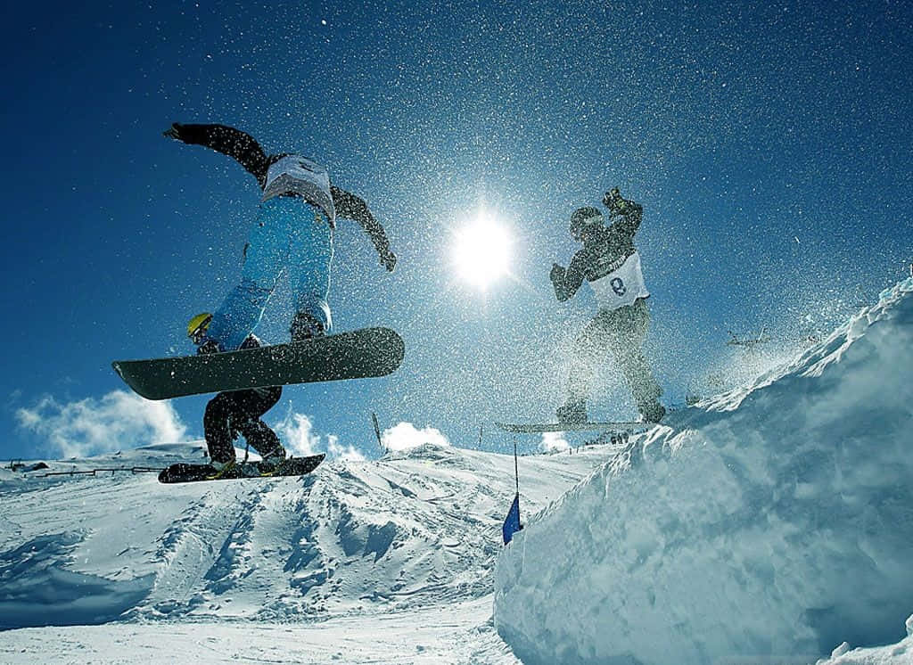 Winter Sports 桌布 壁紙 — 兩名滑雪板運動員在白雪覆蓋的山坡上，迎著熾熱的太陽，在清爽的冬日空氣中翱翔。