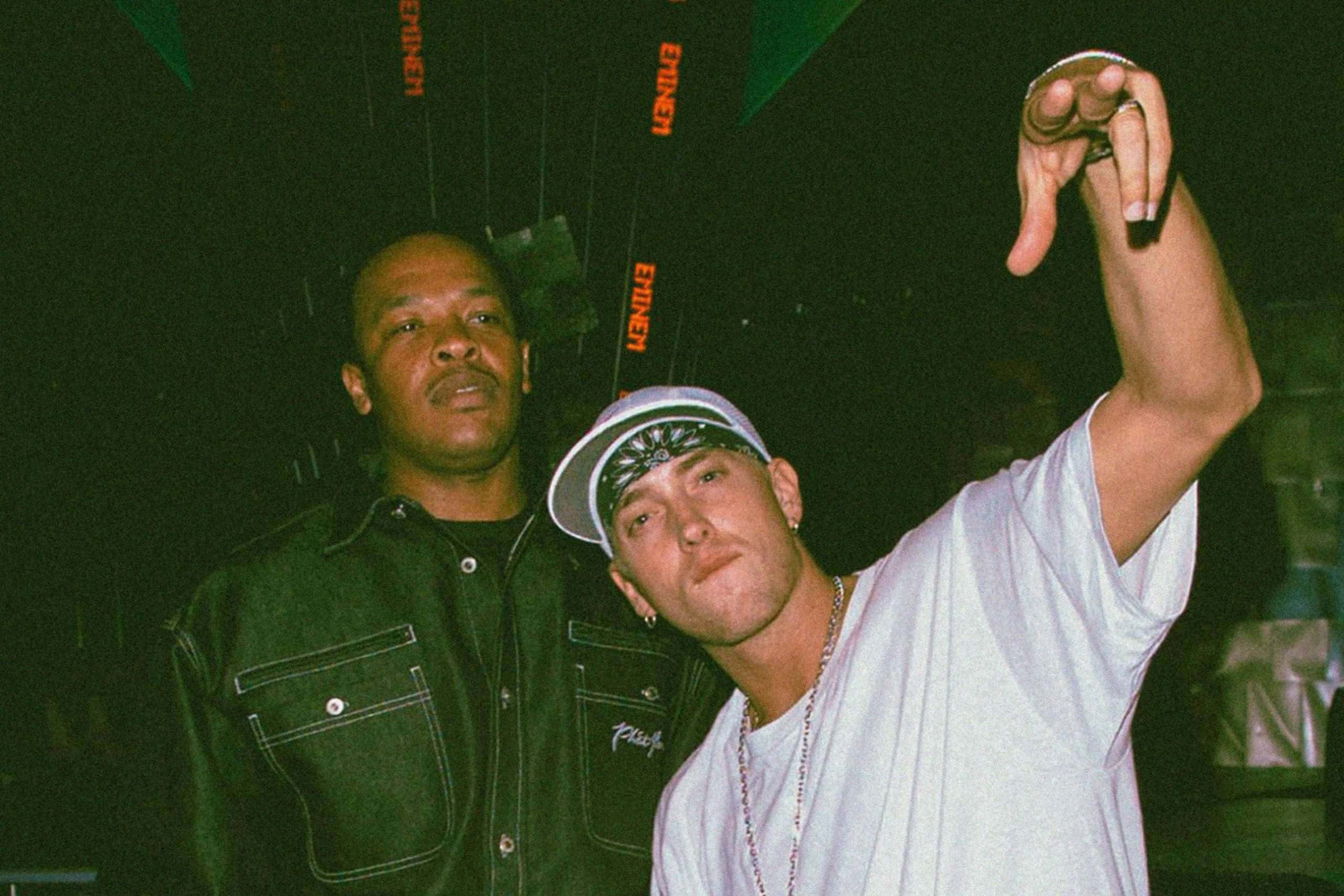Eminem 桌布 壁紙 — 兩名男子在燈光昏暗的場地中擺姿勢，場地有綠色燈光和懸掛的 'Eminem' 橫幅，其中一人舉起戒指。
