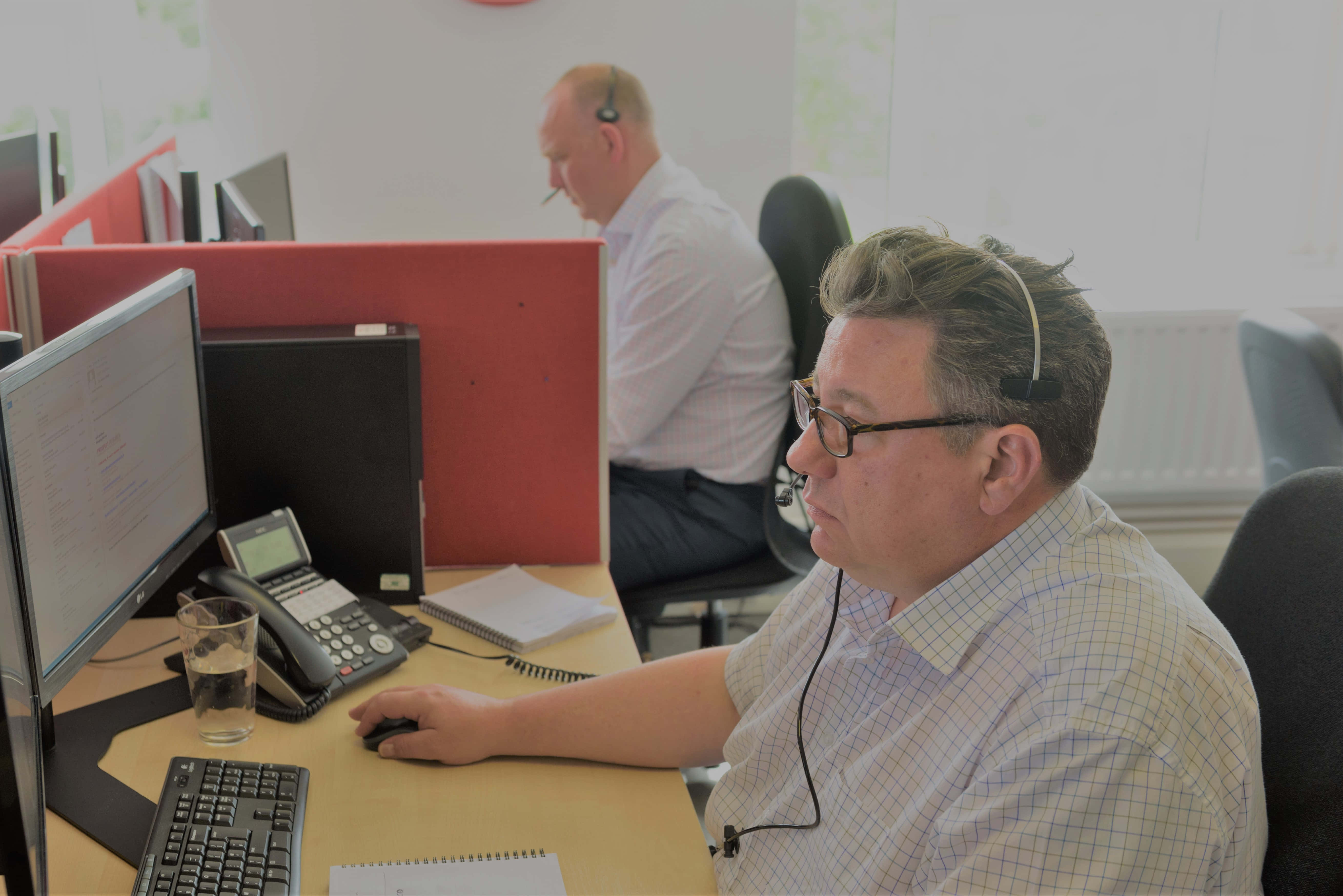 Telemarketing 桌布 壁紙 — 兩名男子在現代辦公室戴著耳機，在設有紅色隔間的電腦工作站工作。