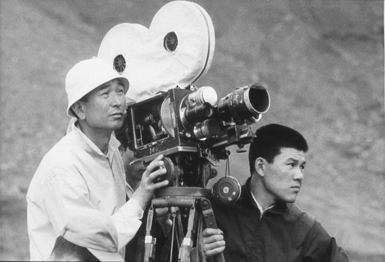 Akira Kurosawa 桌布 壁紙 — 兩名男子操作三腳架上的復古菲林相機，背景是黑白模糊的岩石。