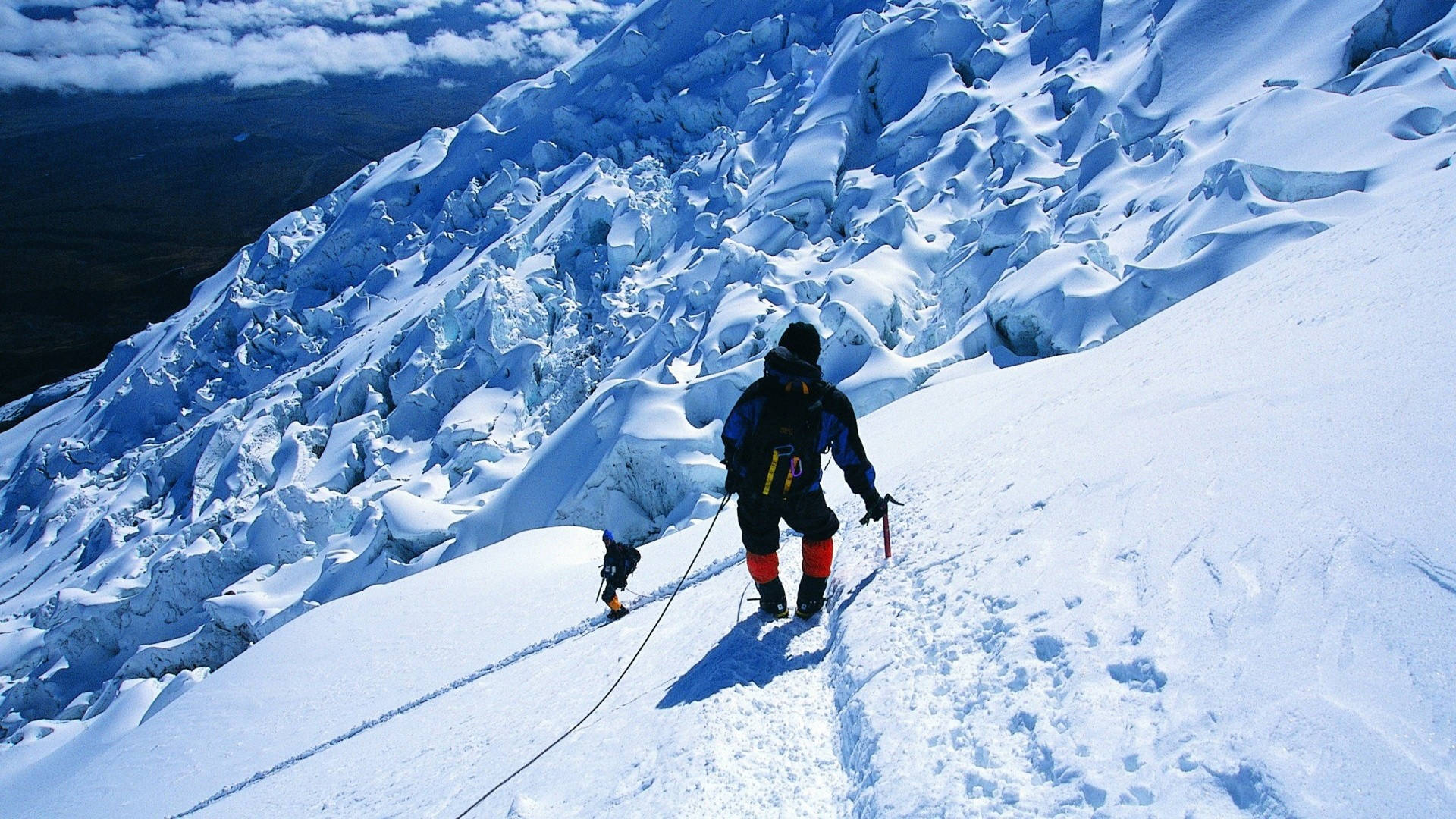 兩名登山者用繩索相連，攀登積雪的冰川斜坡。