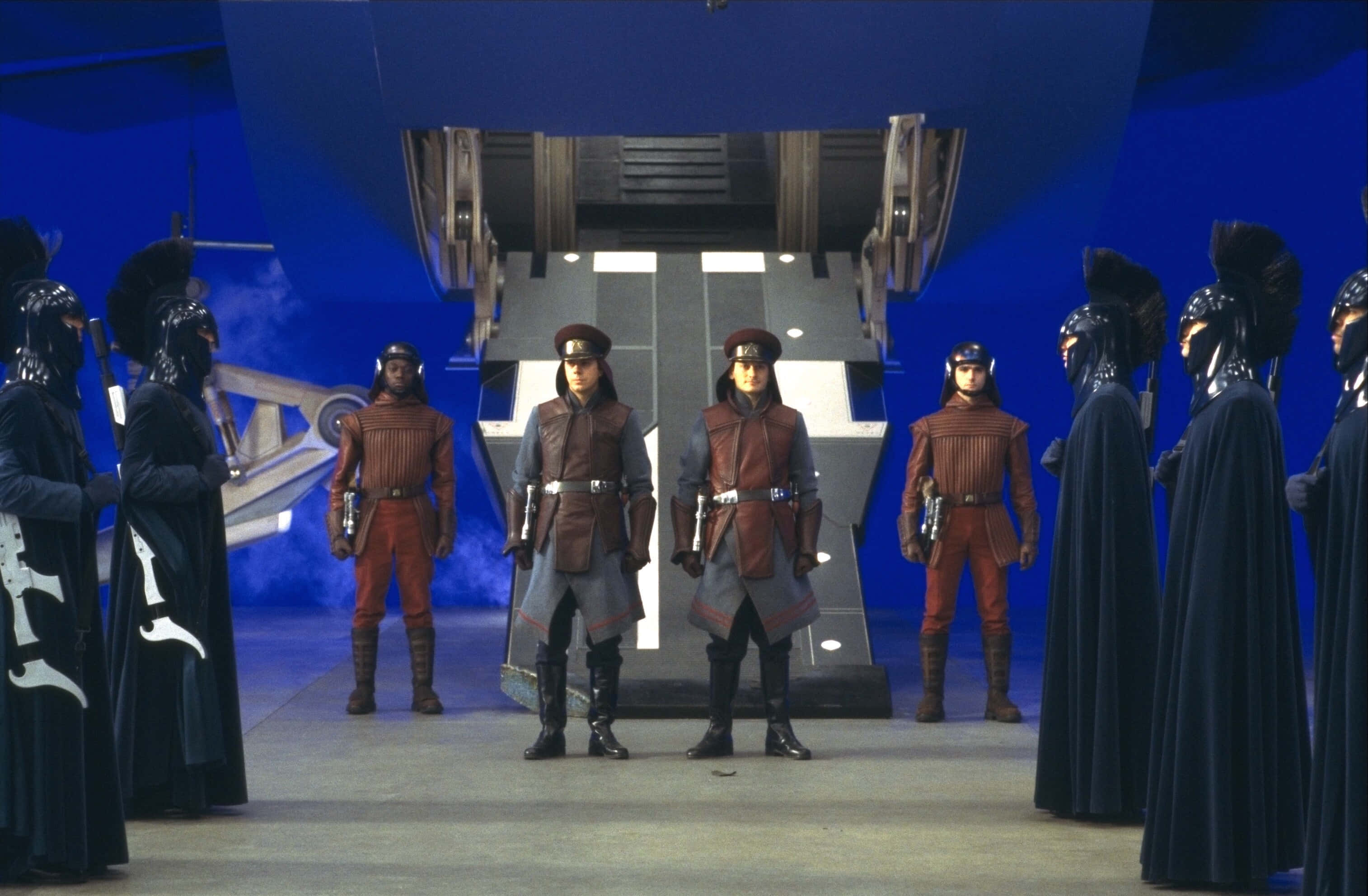 The Phantom Menace 桌布 壁紙 — 兩名絕地武士在未來感十足的藍色燈光機庫中，被身穿黑袍的人物夾在中間立正站好，上方有一艘太空船。
