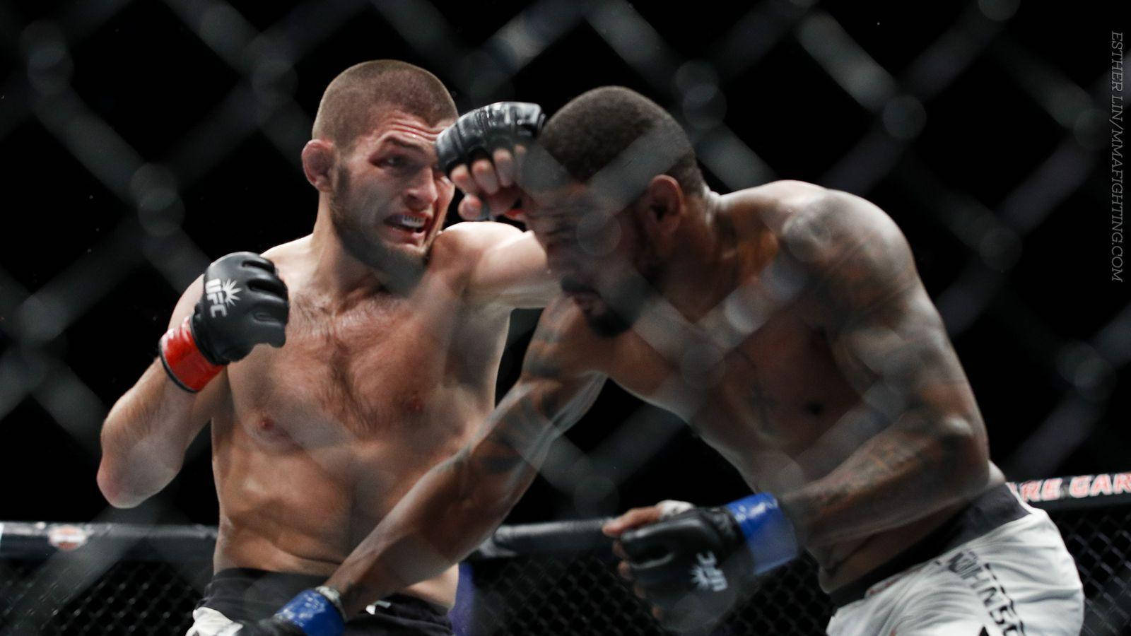 UFC 桌布 壁紙 — 兩名肌肉發達的拳手在籠中激戰，其中一人在明亮的場館燈光下向對手面部揮出強力一拳。