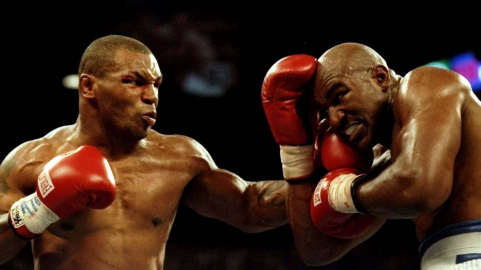 mike tyson 桌布 壁紙 — 兩名肌肉發達的拳擊手在戲劇性的擂台上碰撞，紅色手套和汗水在明亮燈光下閃閃發光。